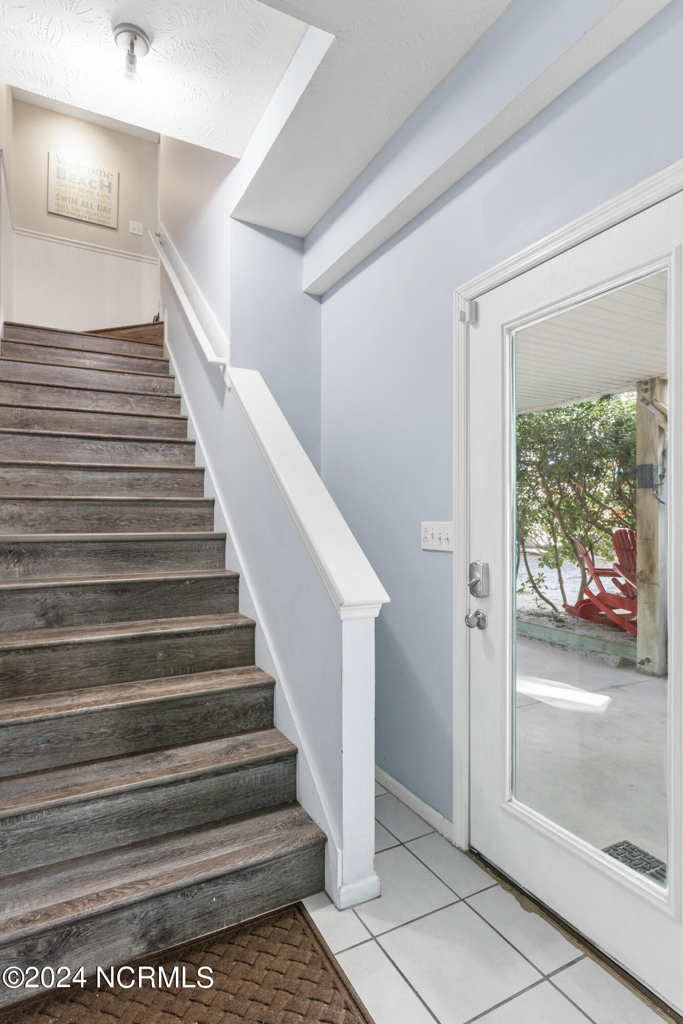 Entryway staircase beside a glass door opening onto a patio with red chairs.