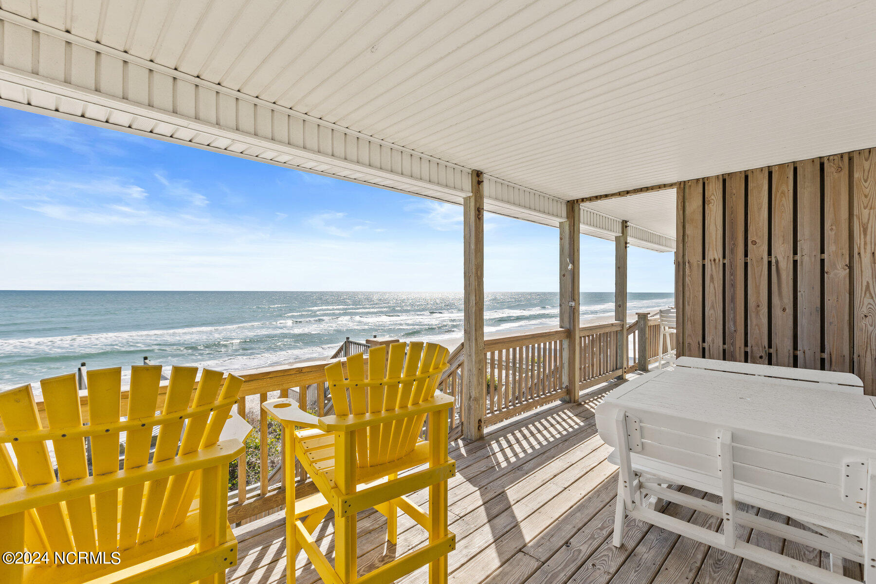 Covered oceanfront deck with yellow Adirondack chairs and sweeping beach views.