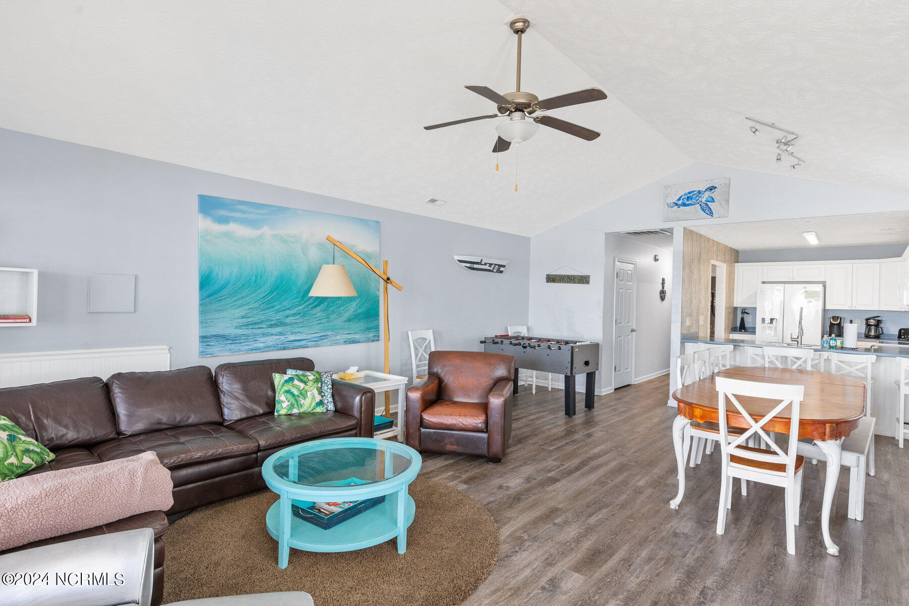 Open-plan living room with leather sofa, turquoise coffee table, and ocean-wave artwork beside the dining area.
