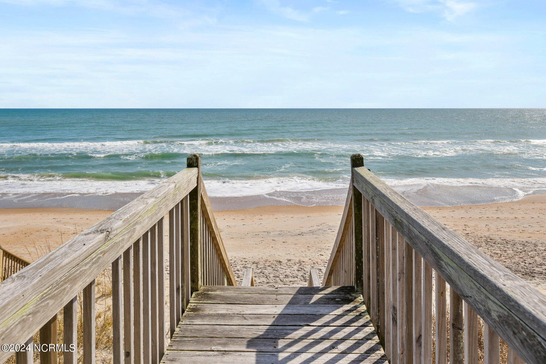 Wooden beach stairs lead down to a sandy shore and ocean.