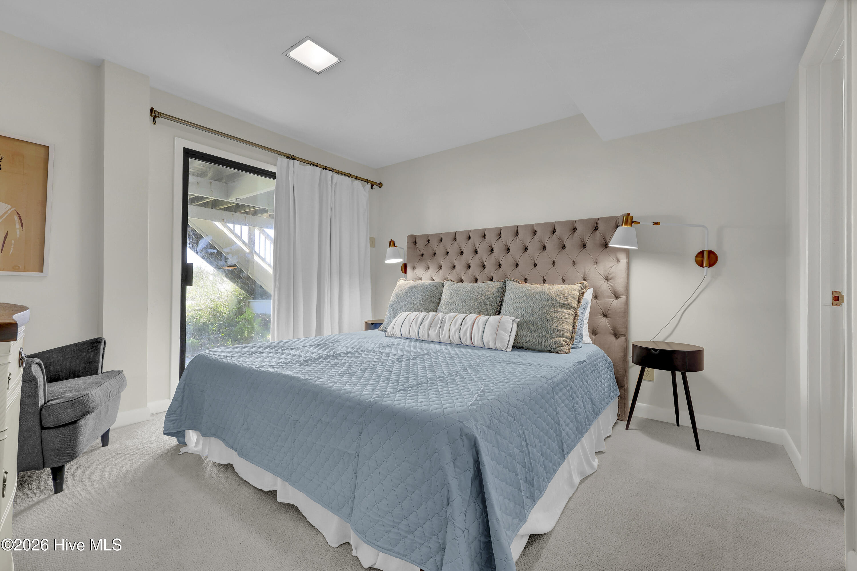 Furnished bedroom with a blue-quilted bed, tufted headboard, and glass door with white curtains.