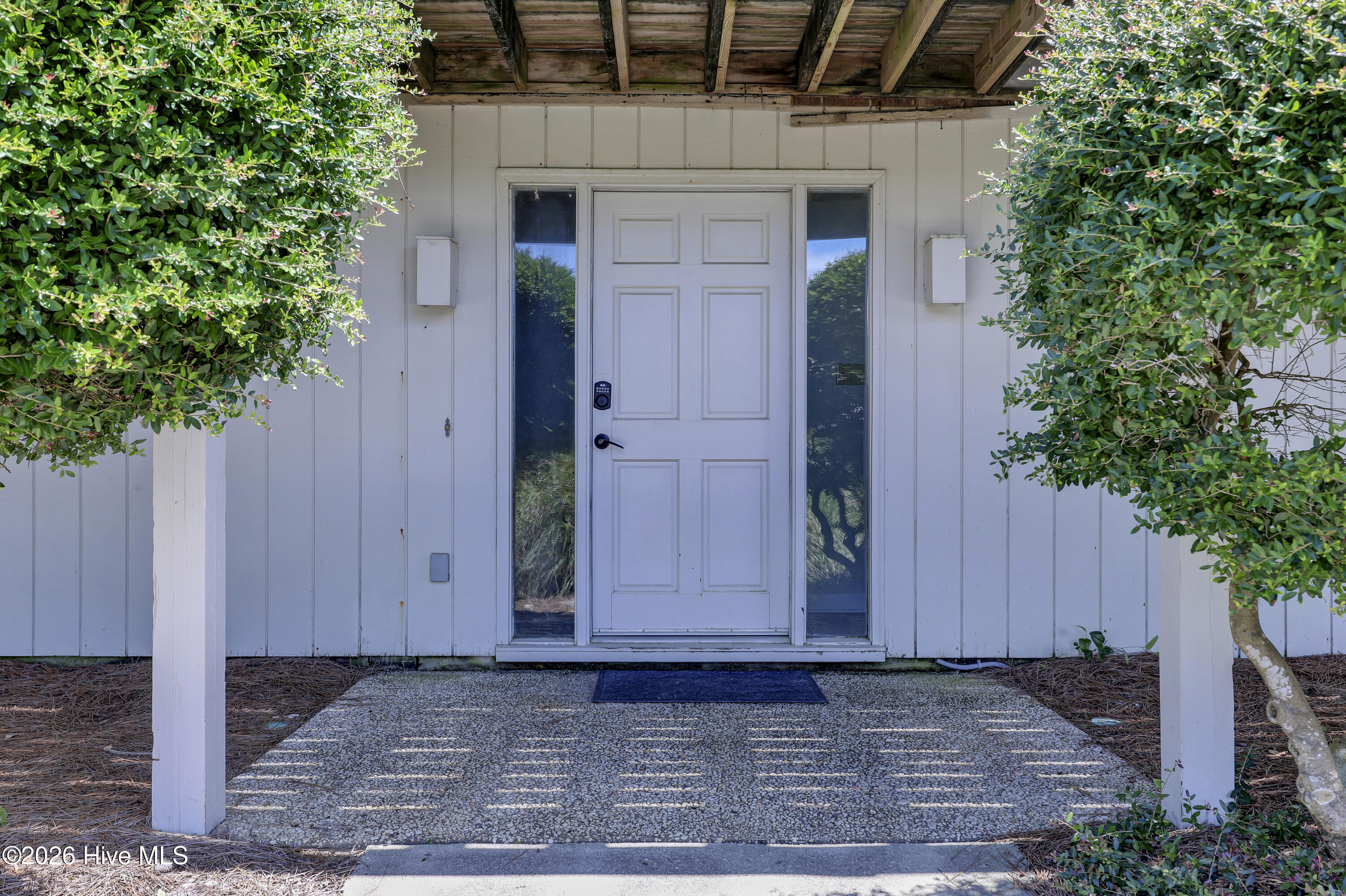 White front entry with glass sidelights beneath a covered porch, framed by shrubs.