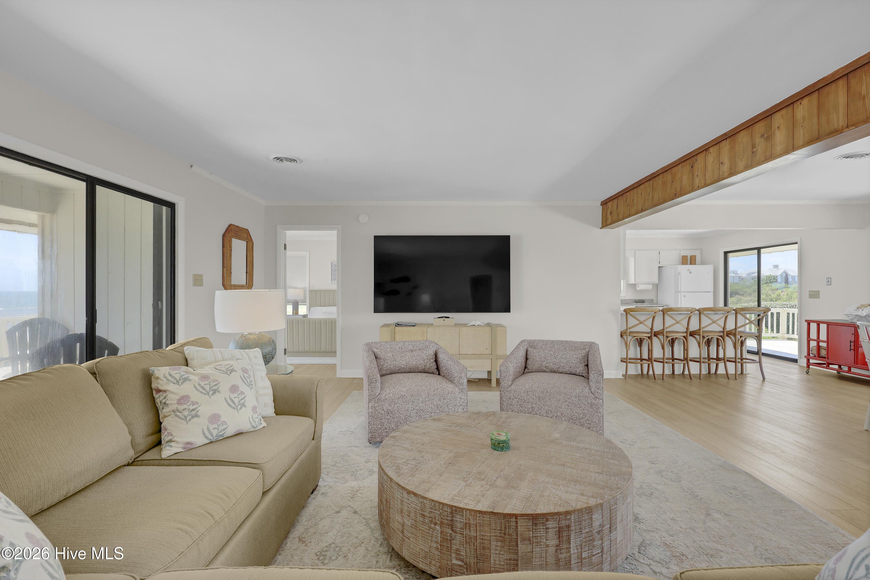 Living room with beige sofa, round wood coffee table, and a glimpse of water through sliding glass doors.