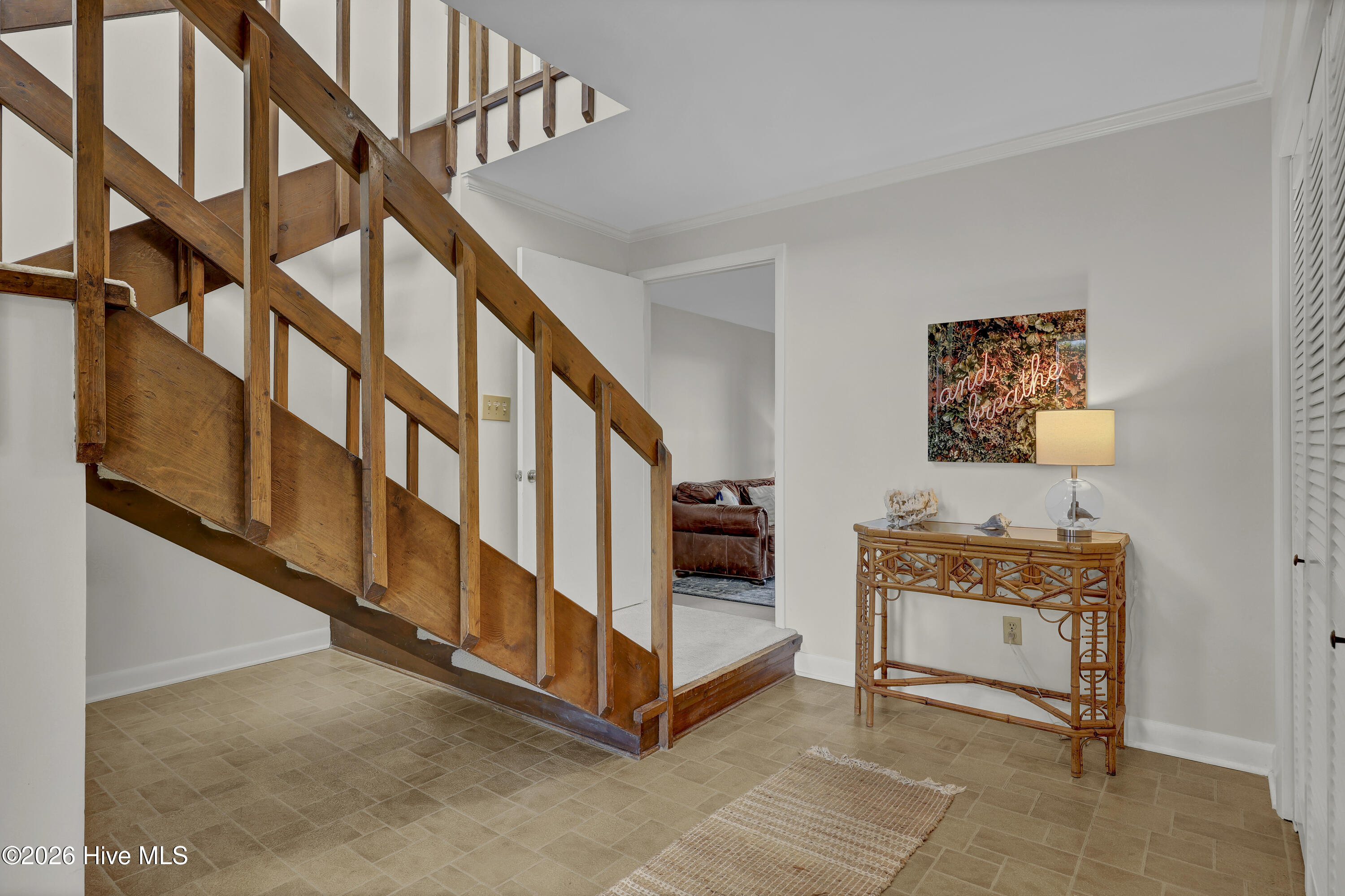 Entryway with a rustic wooden staircase, tiled floor, and woven console table.
