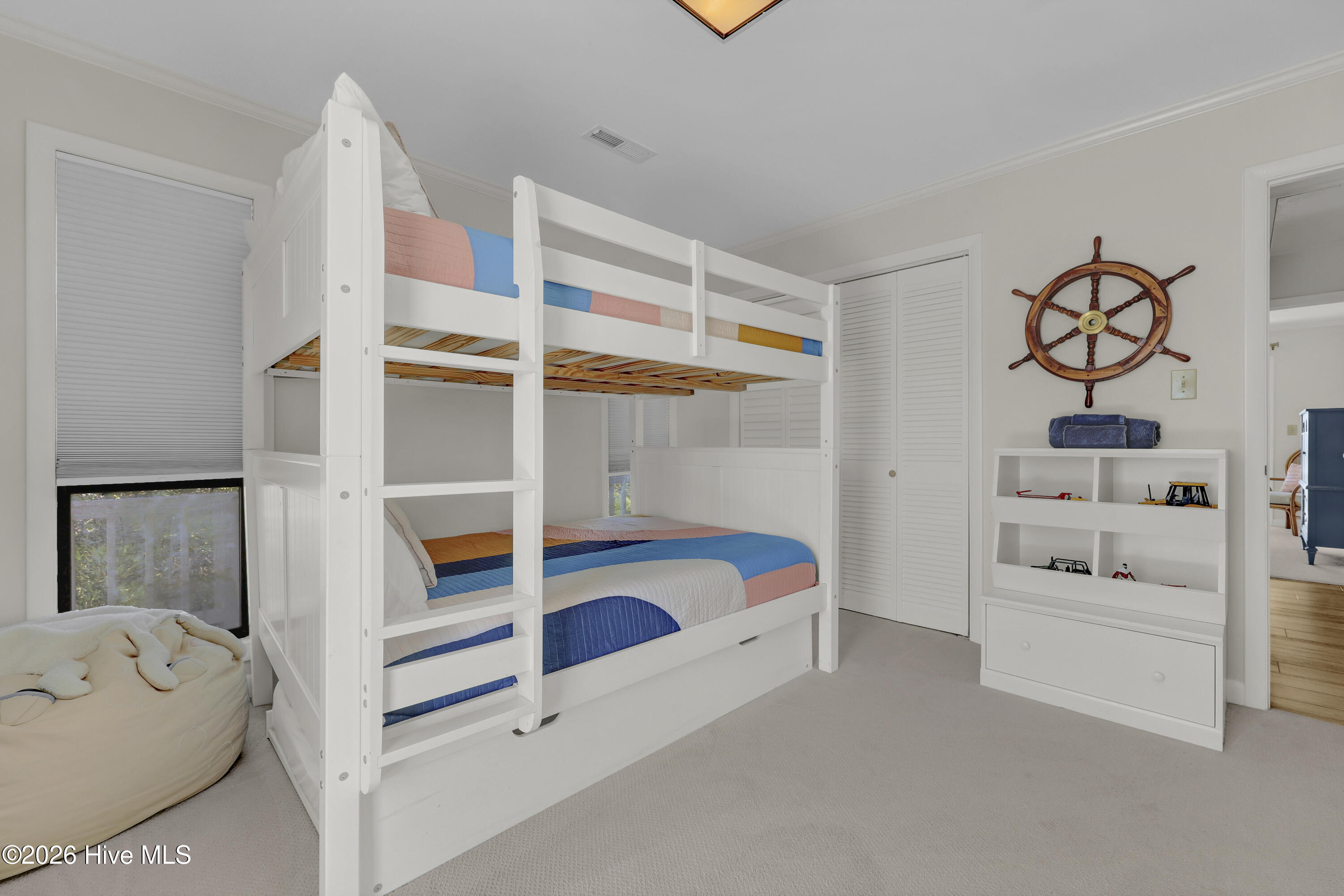 Bedroom with a white bunk bed, colorful bedding, a ship’s wheel, and a toy shelf.