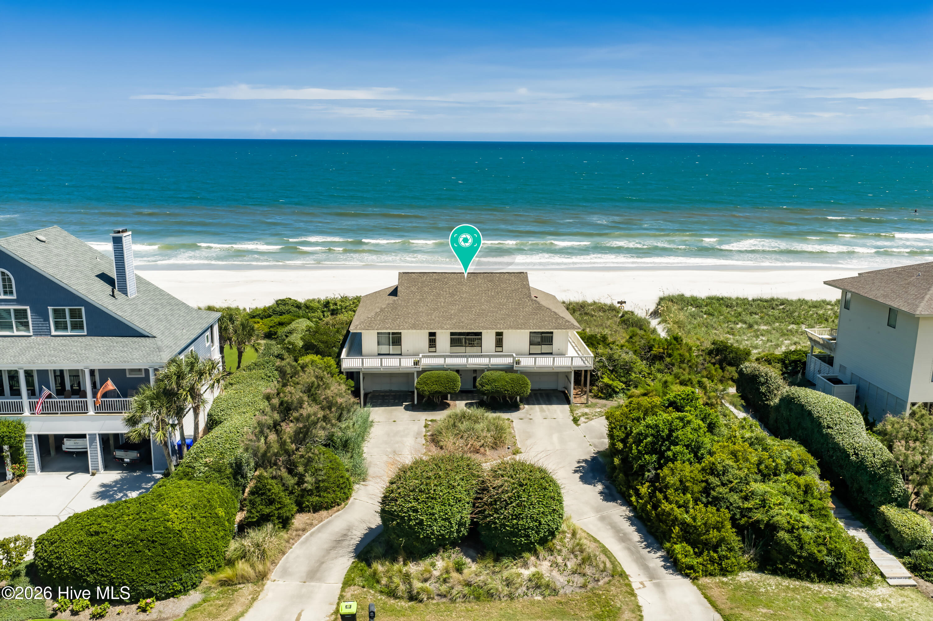 Aerial view of a beachside house with landscaped grounds, neighboring homes, and ocean beyond.