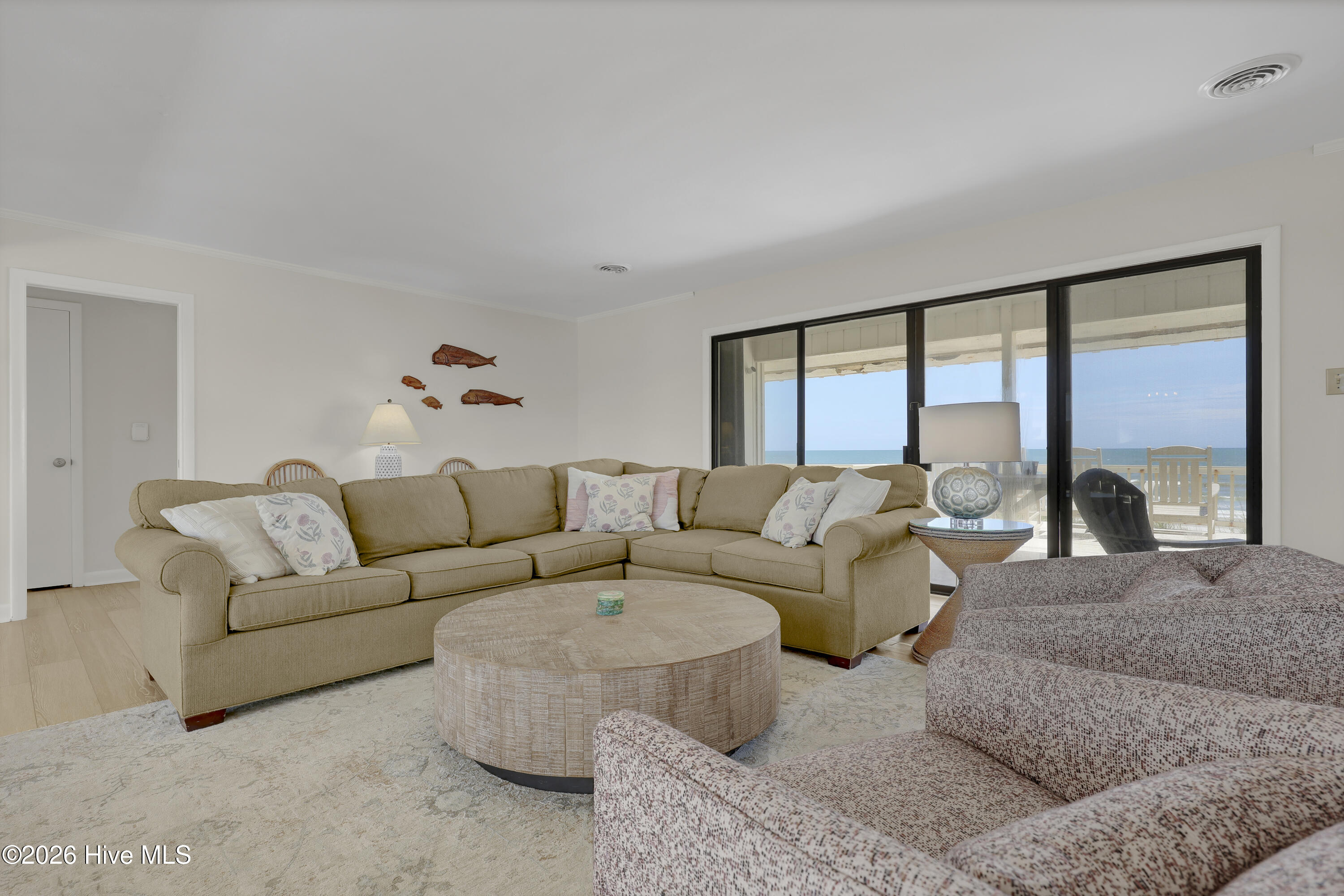 Furnished living room with a tan sectional and sliding doors overlooking the ocean.