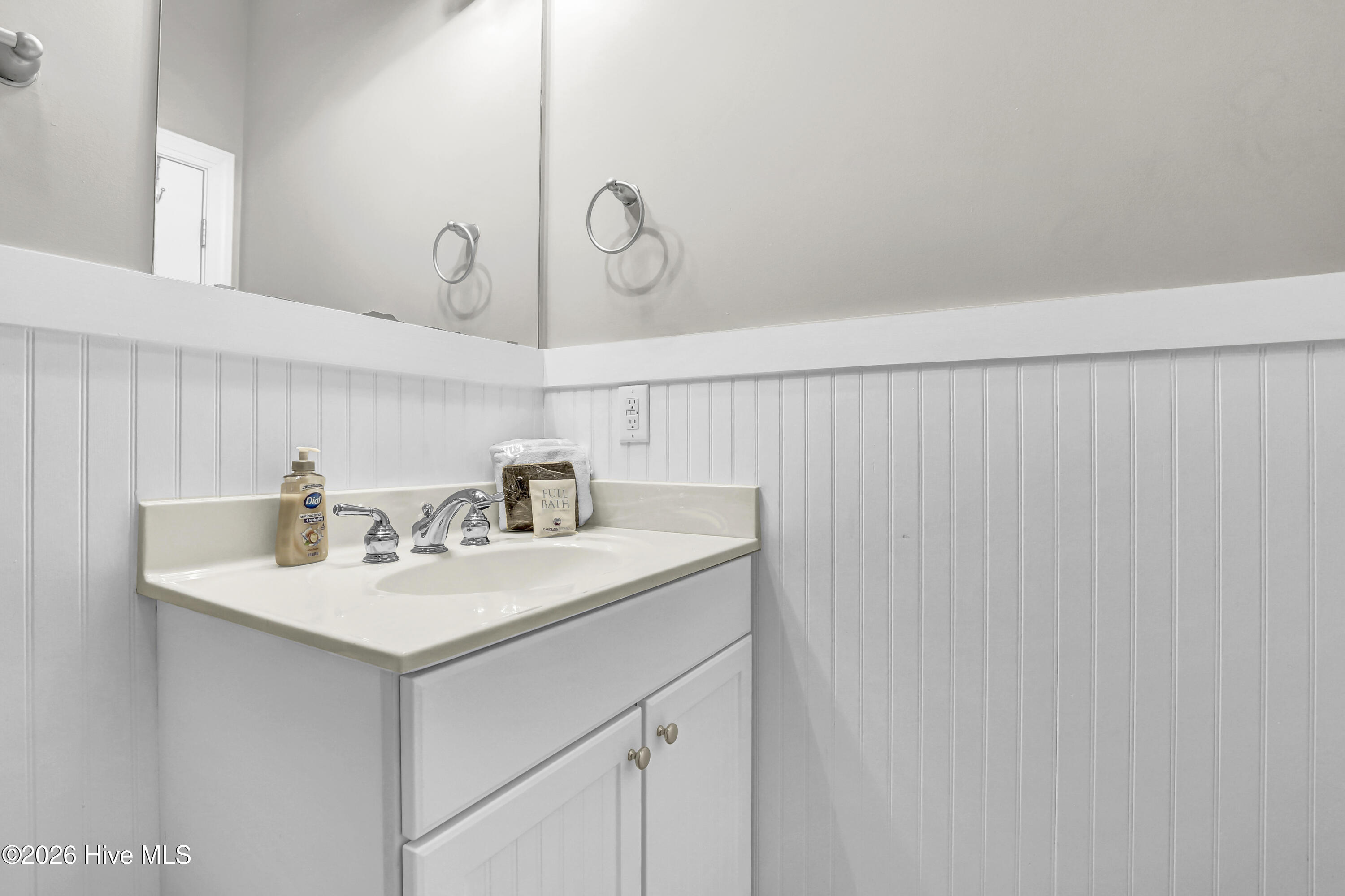 Bathroom vanity with a white sink, chrome faucet, large mirror, and beadboard wainscoting.