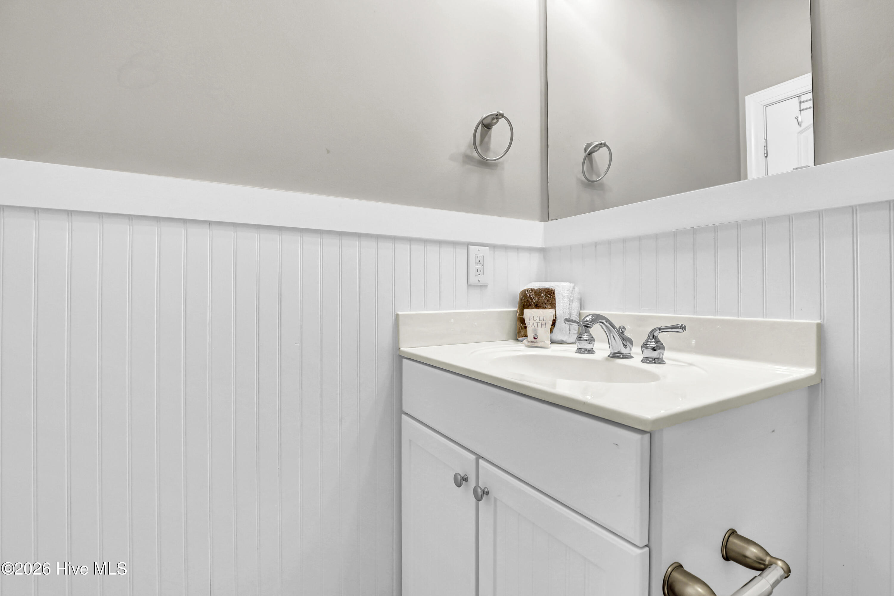 Bathroom vanity with white beadboard, mirrored medicine cabinet, and chrome faucet.