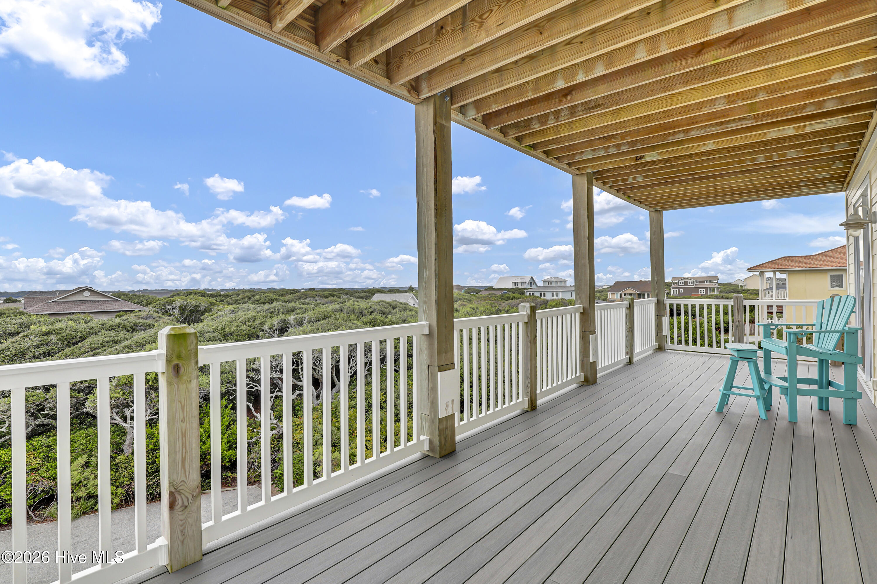 Covered deck with turquoise Adirondack chairs overlooking coastal vegetation and neighboring homes.