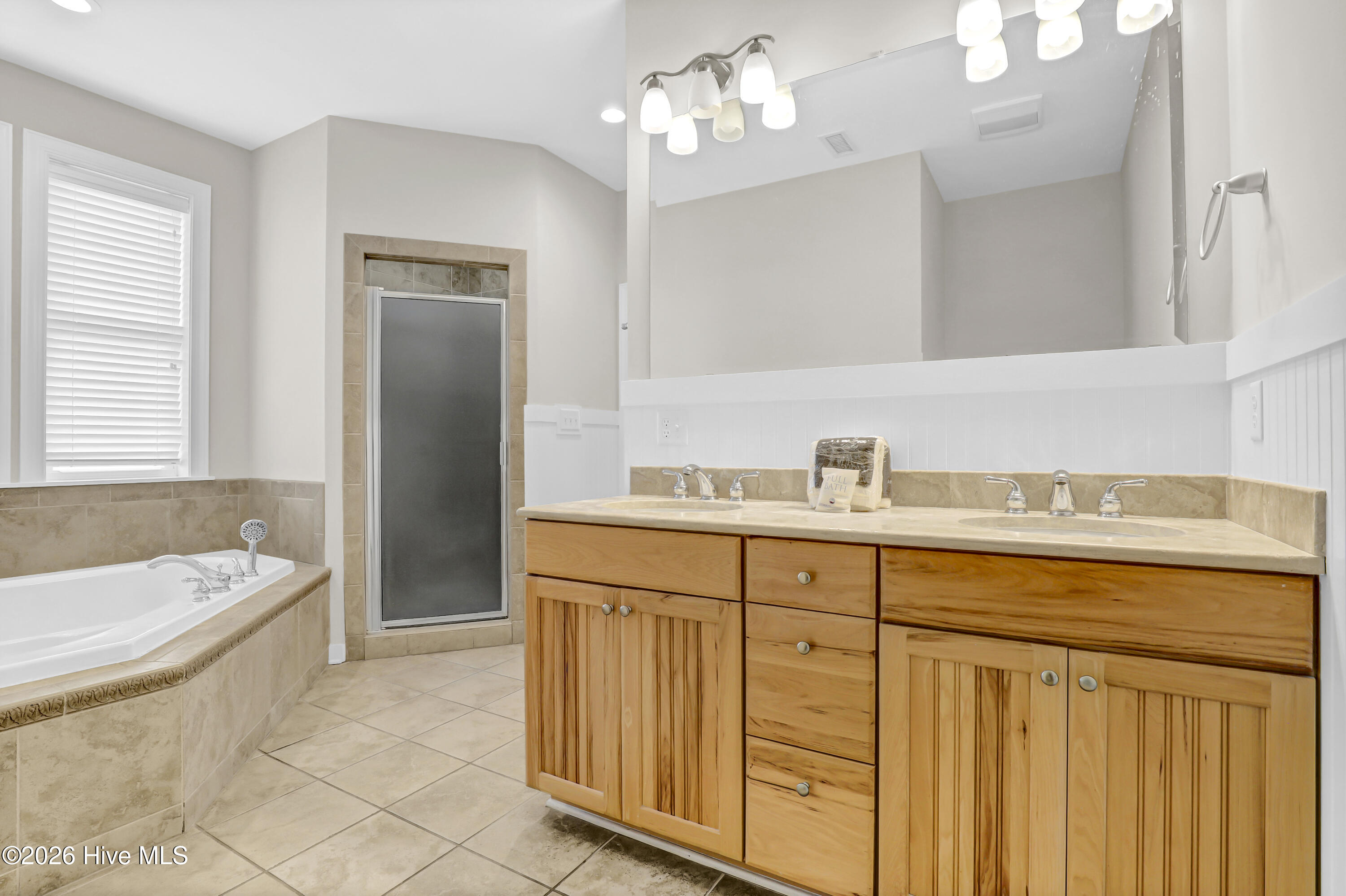 Bathroom with a double-sink wood vanity, built-in soaking tub, and glass-enclosed shower.