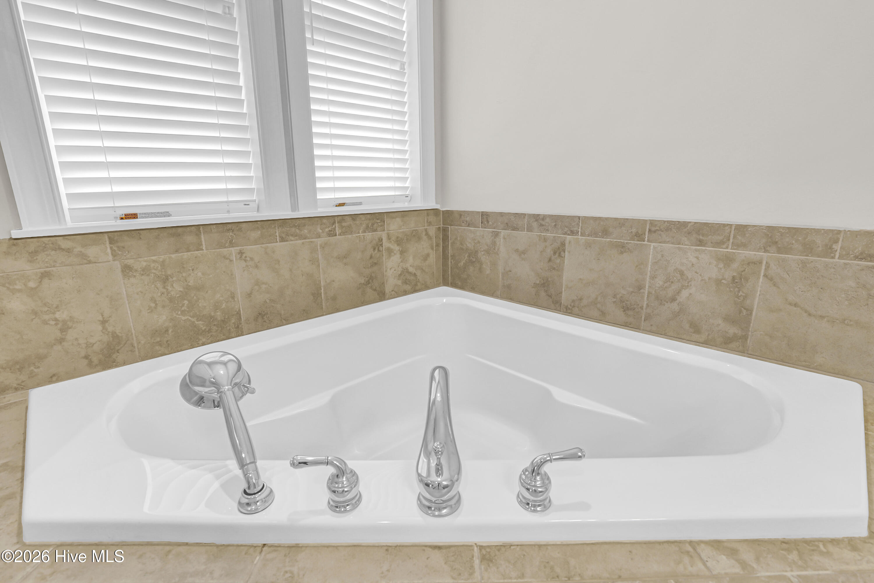 White soaking tub with chrome fixtures beneath windows with blinds