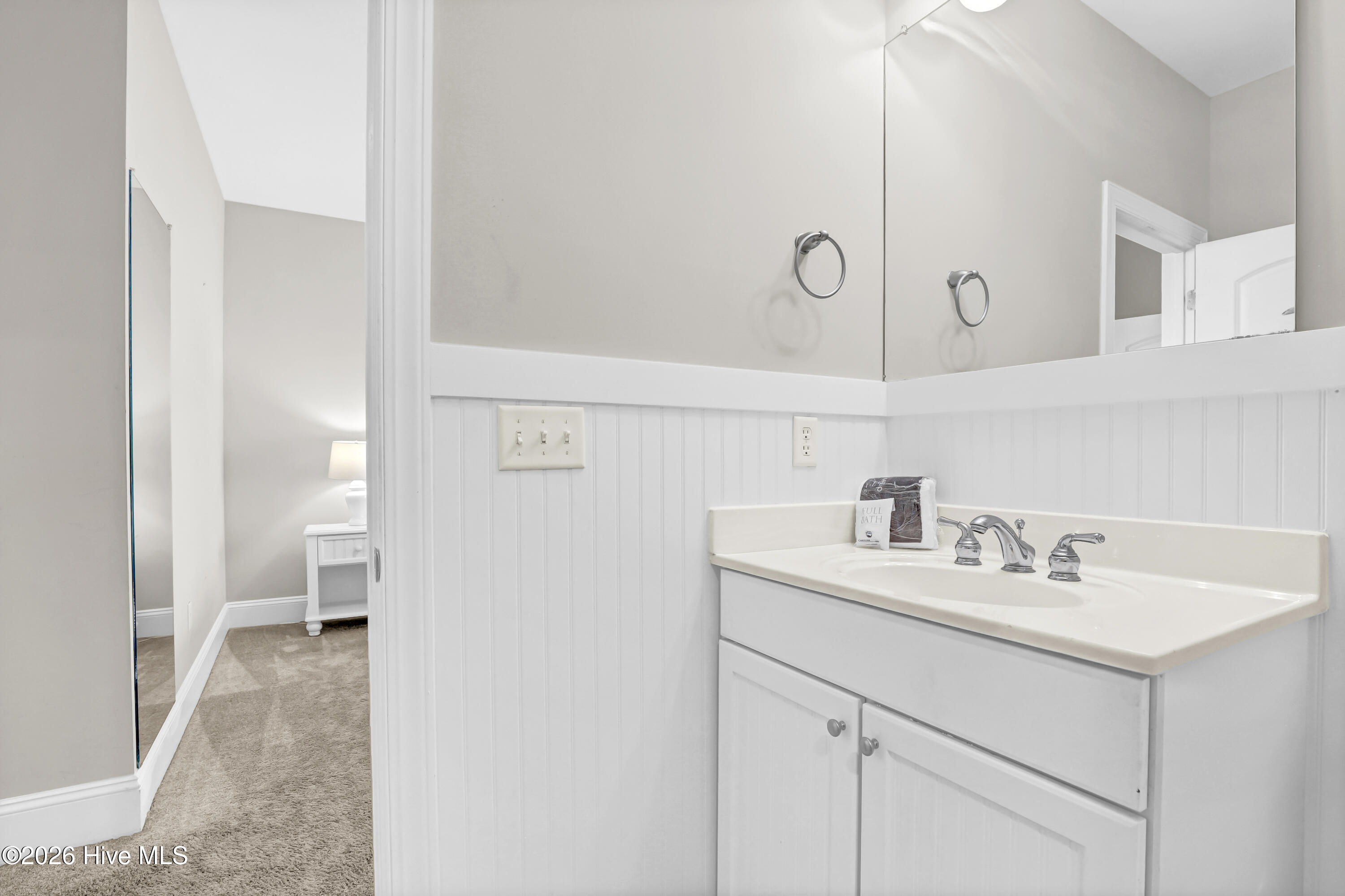 Bathroom vanity with a large mirror and white beadboard wainscoting beside a carpeted dressing area.