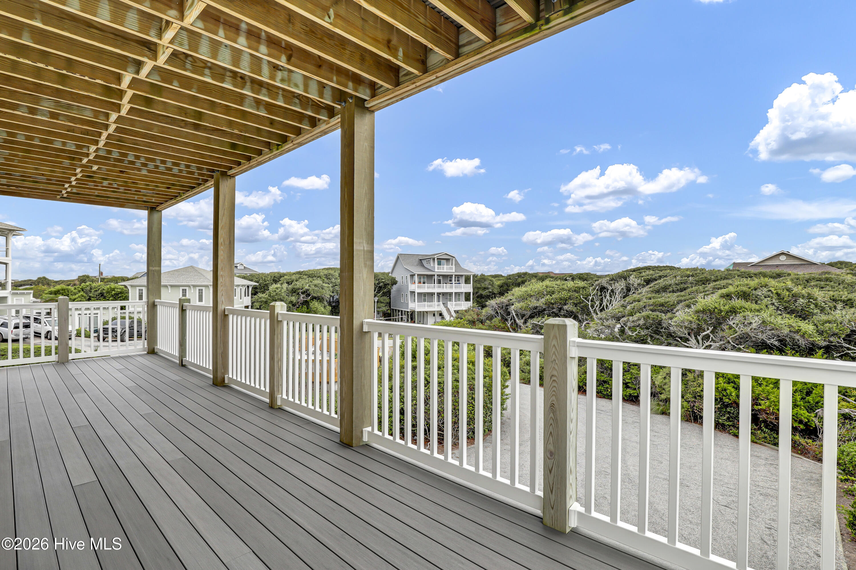 Covered deck with white railings and exposed wood framing overlooking coastal greenery and nearby homes.
