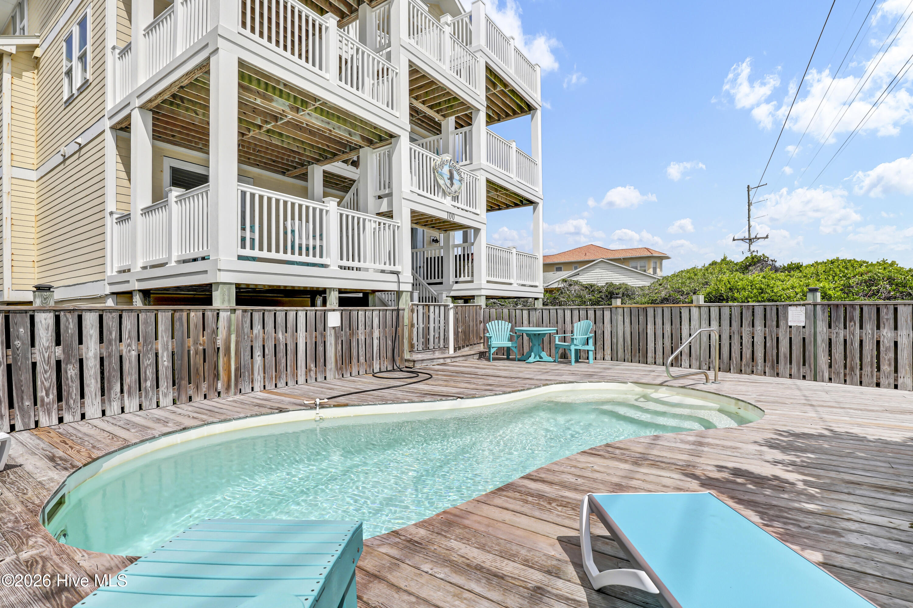 Coastal home with white balconies overlooking a curved pool and turquoise poolside seating.