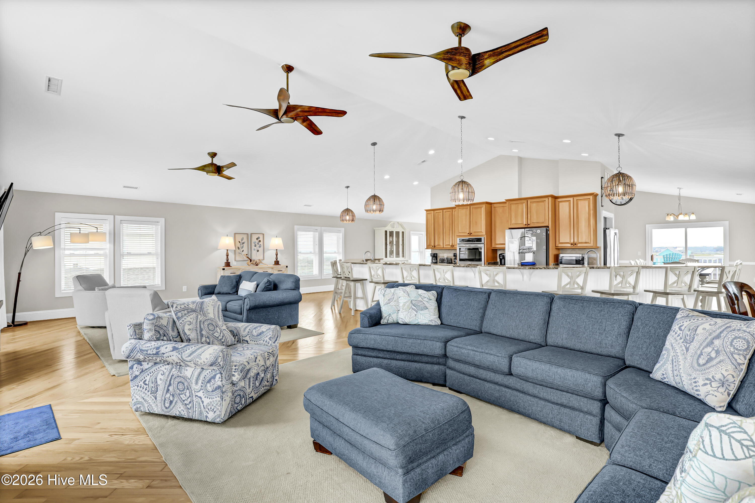 Open-plan living room and kitchen with blue sofas, patterned armchairs, and a long island with bar stools.