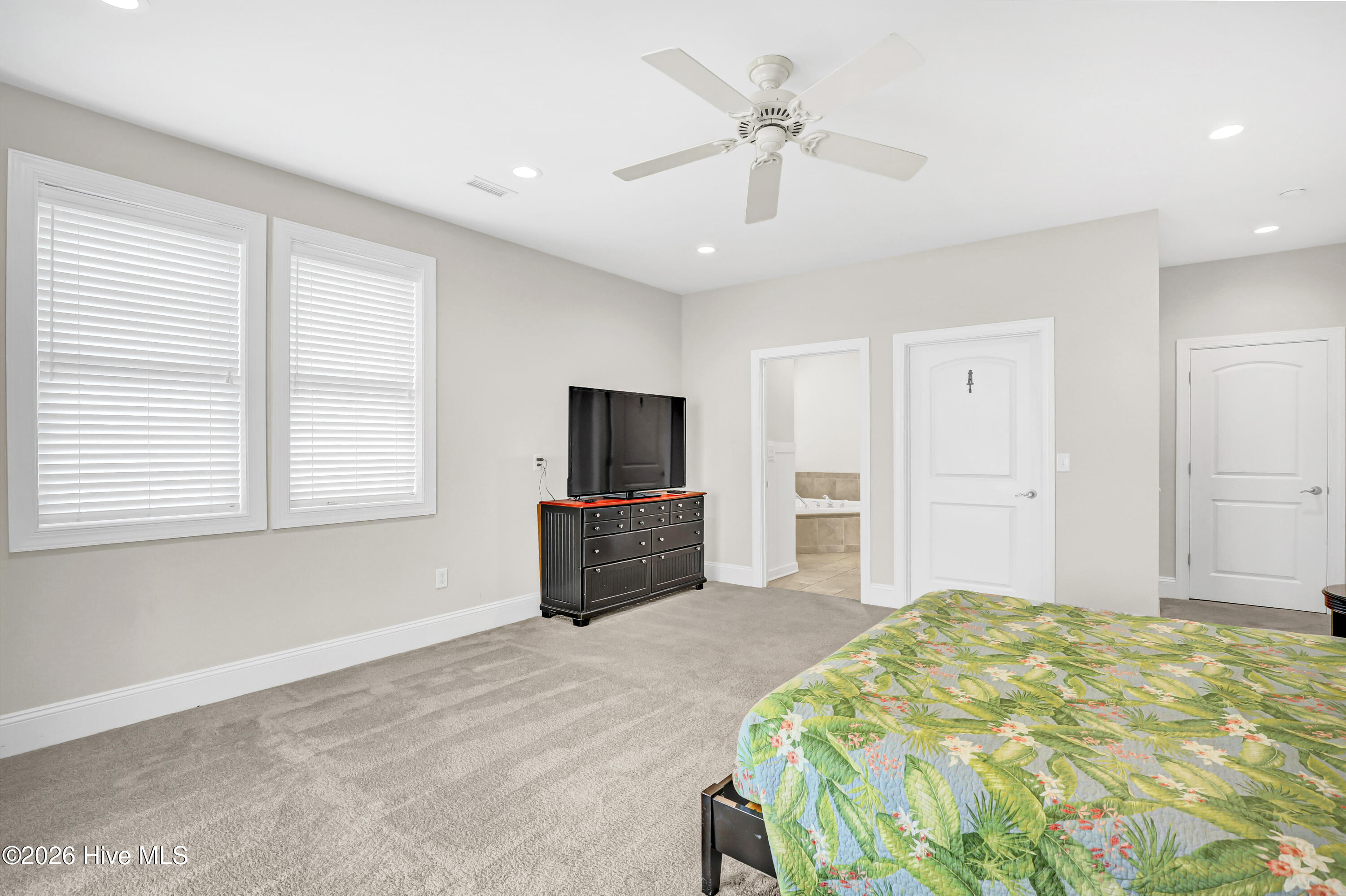 Bedroom with tropical bedspread, ceiling fan, and television on a dresser.