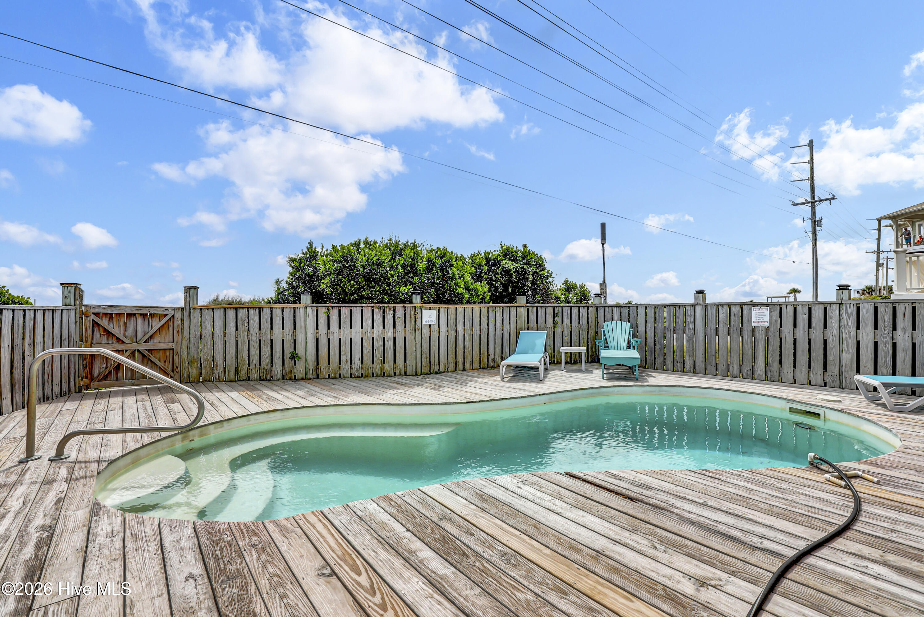 Outdoor pool with a weathered wooden deck, privacy fence, and turquoise lounge chairs.