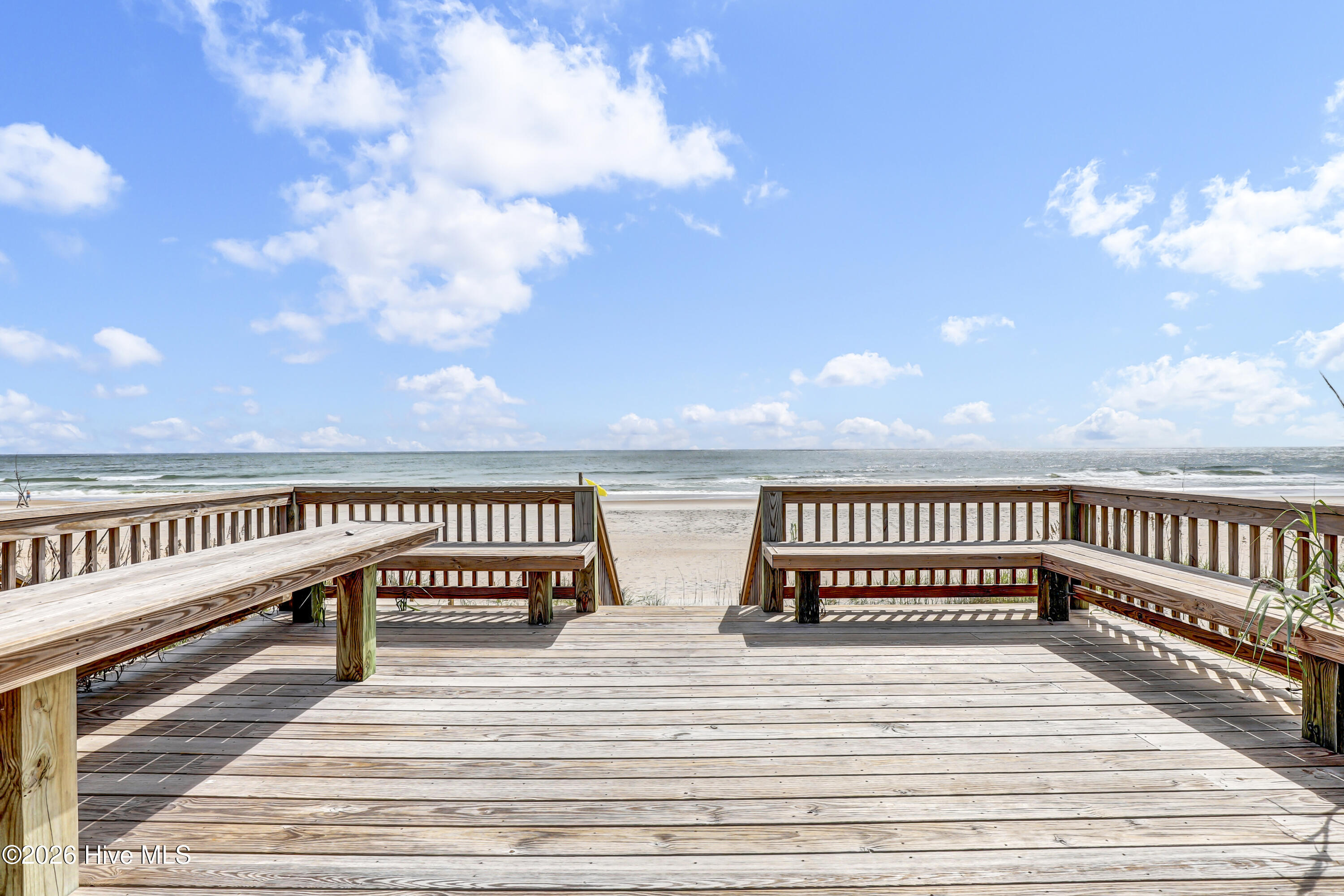 Wooden beach deck with built-in benches overlooking the ocean and sandy shore.