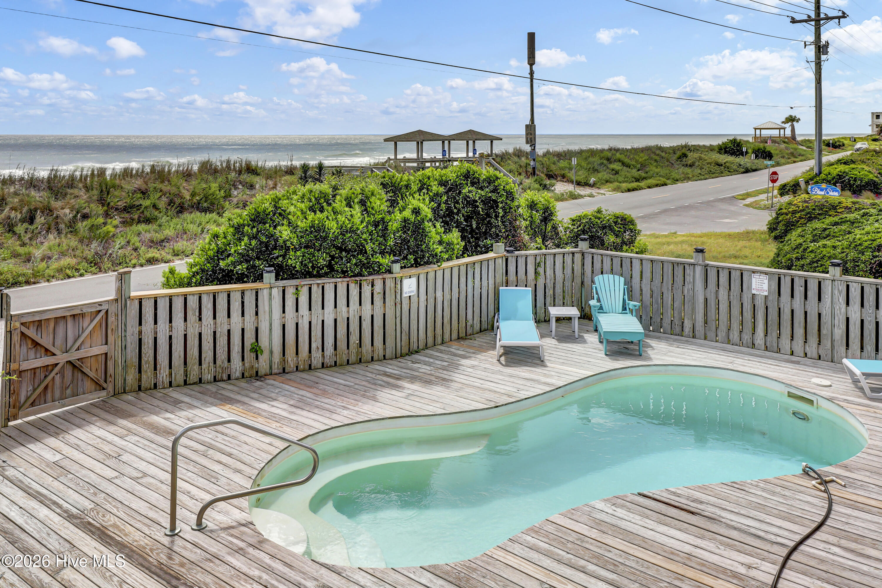 Backyard pool and wood deck overlooking the ocean, with turquoise lounge chairs.