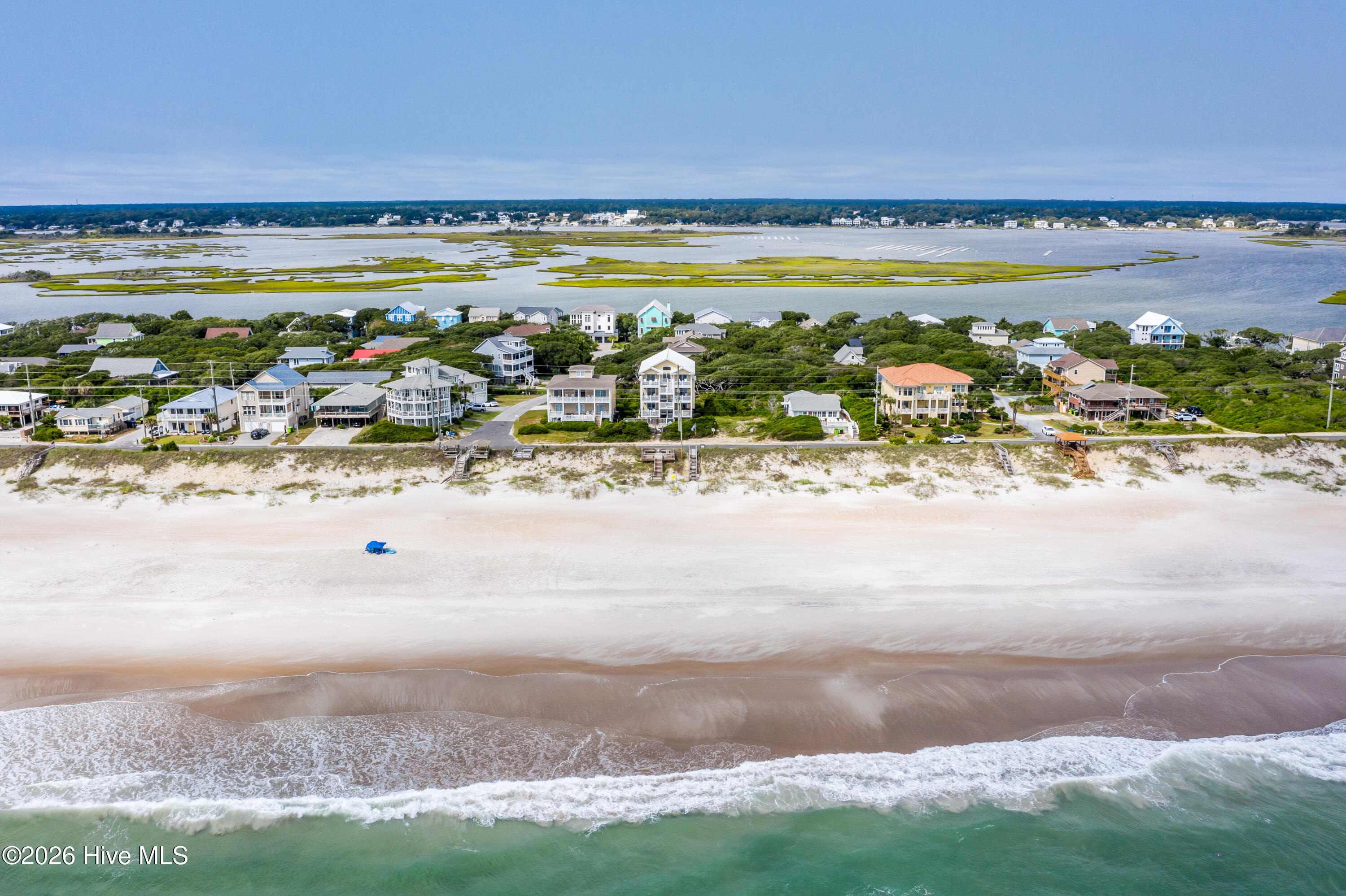 Aerial view of beachfront homes, sandy shore, ocean surf, and a marsh inlet.
