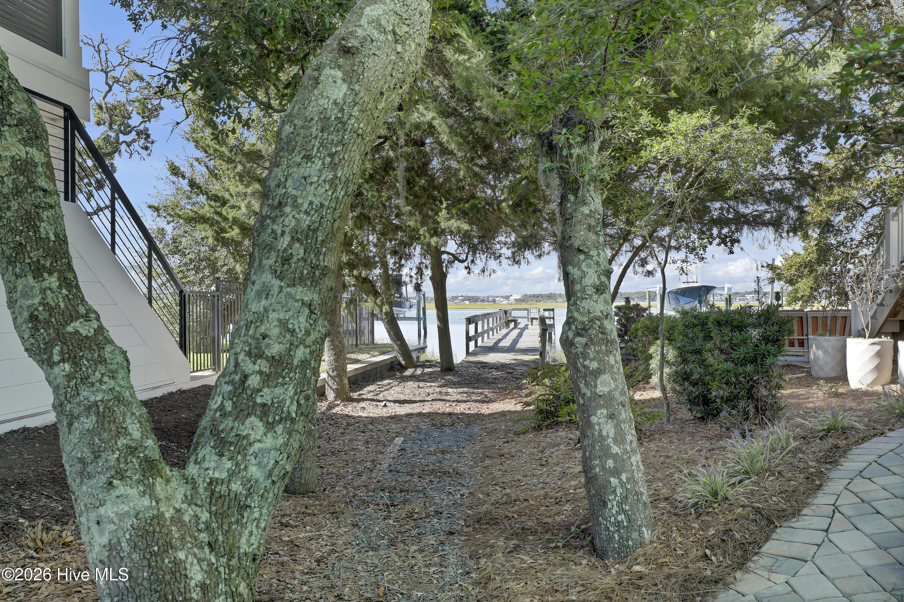 Waterfront yard with a wooden dock beneath mature trees.