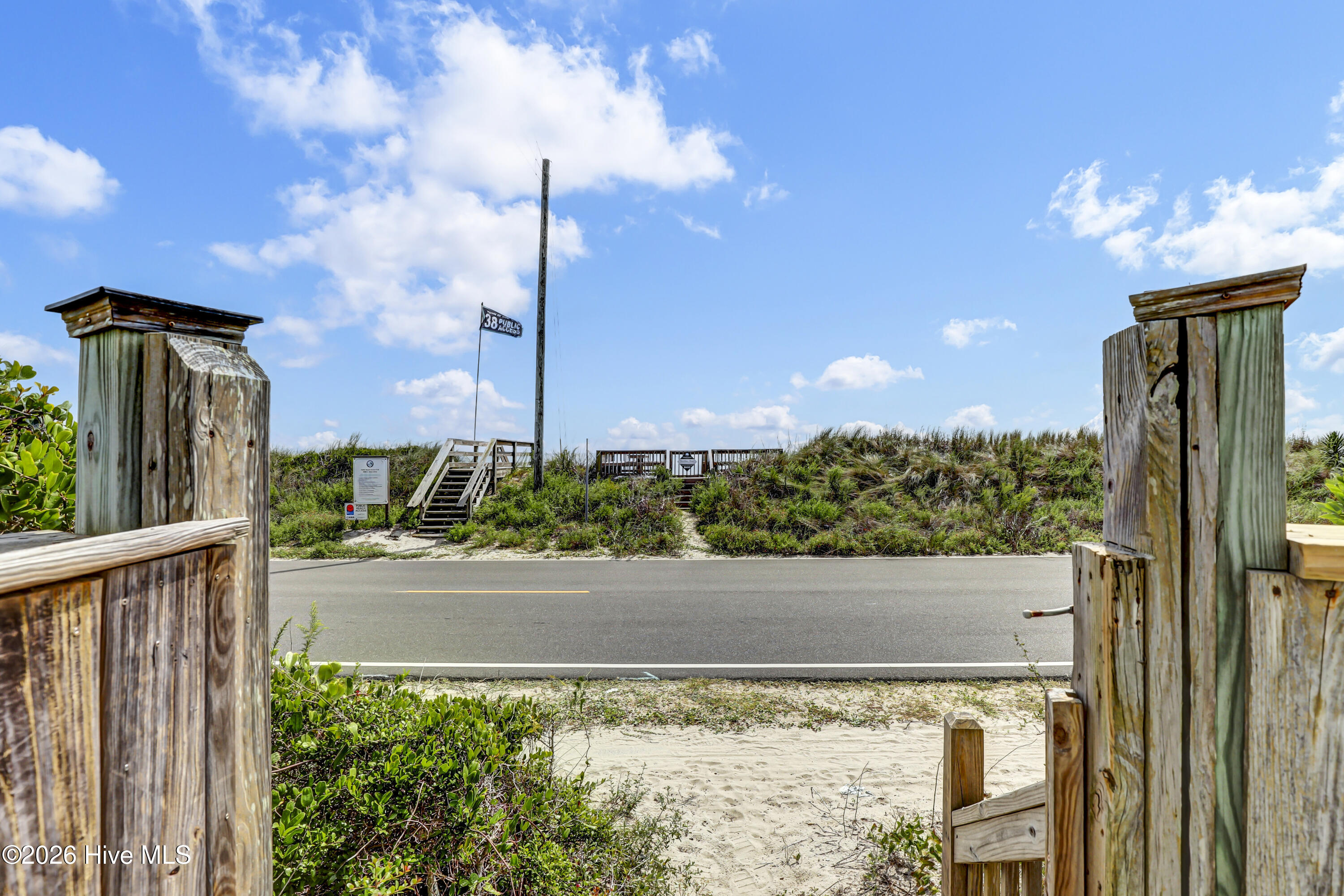 Beach access gate opening onto a sandy path, with dune stairs and a public access sign across the road.