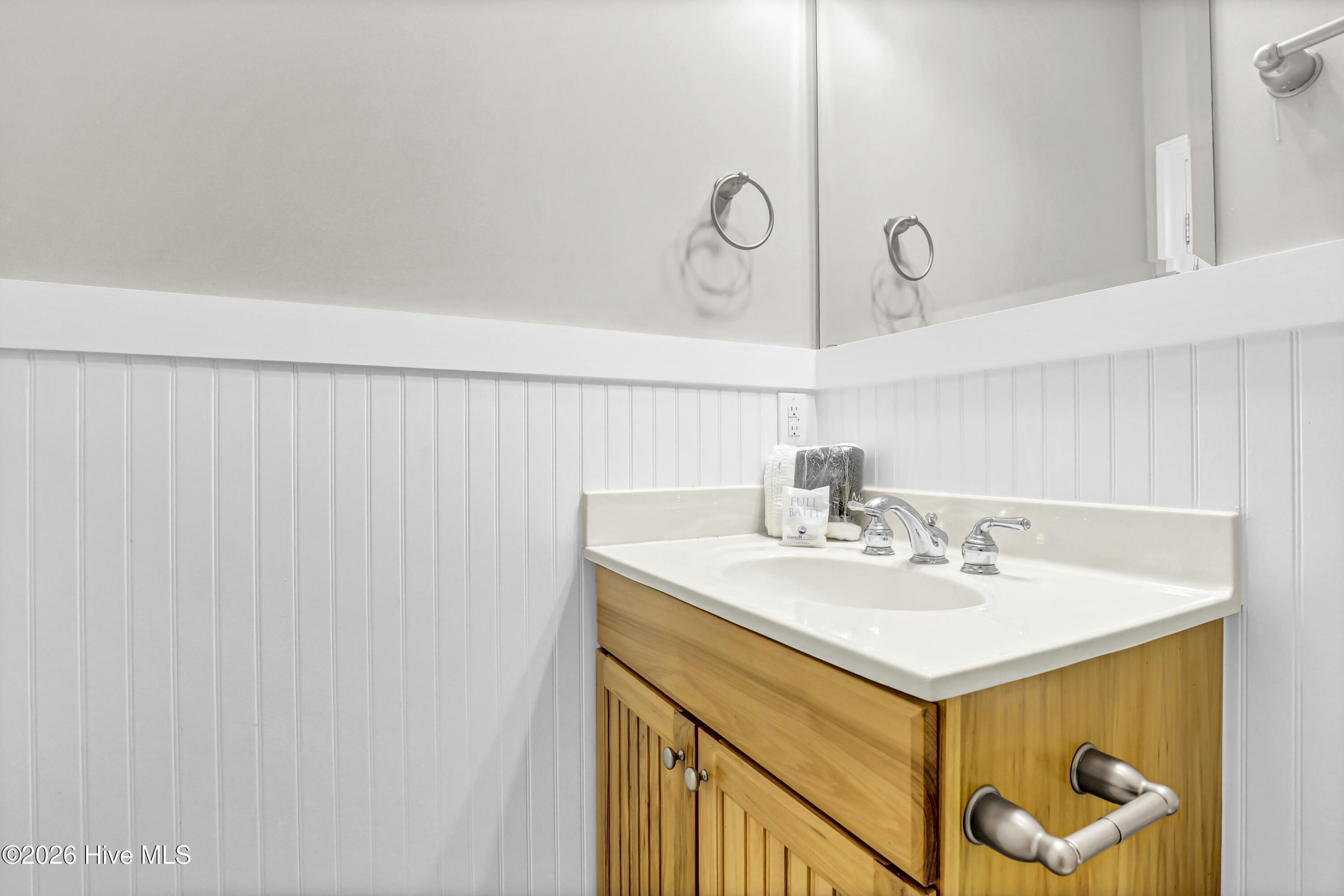 Bathroom vanity with a honey-colored wood cabinet, white sink, chrome faucet, and mirrored wall.