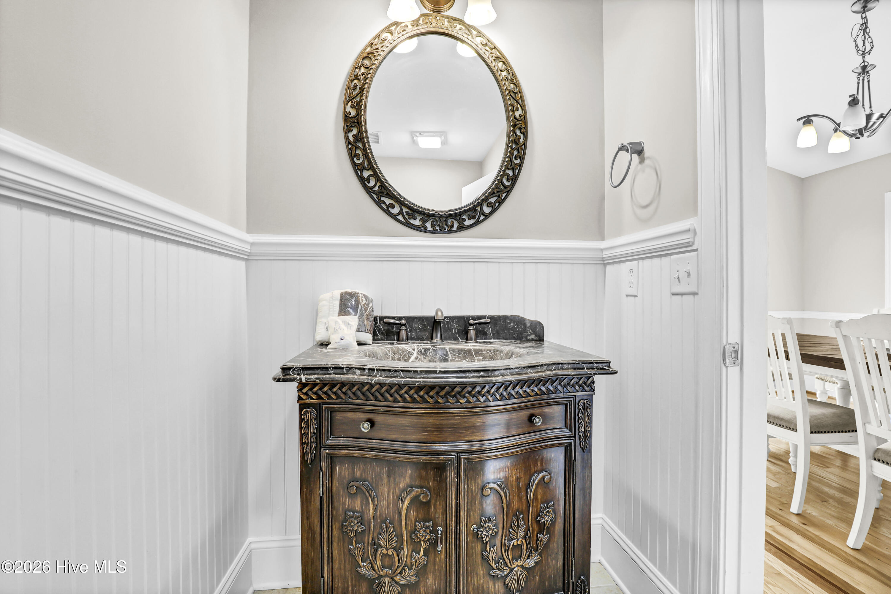 Bathroom vanity with a marble sink, ornate dark wood cabinet, and oval mirror.