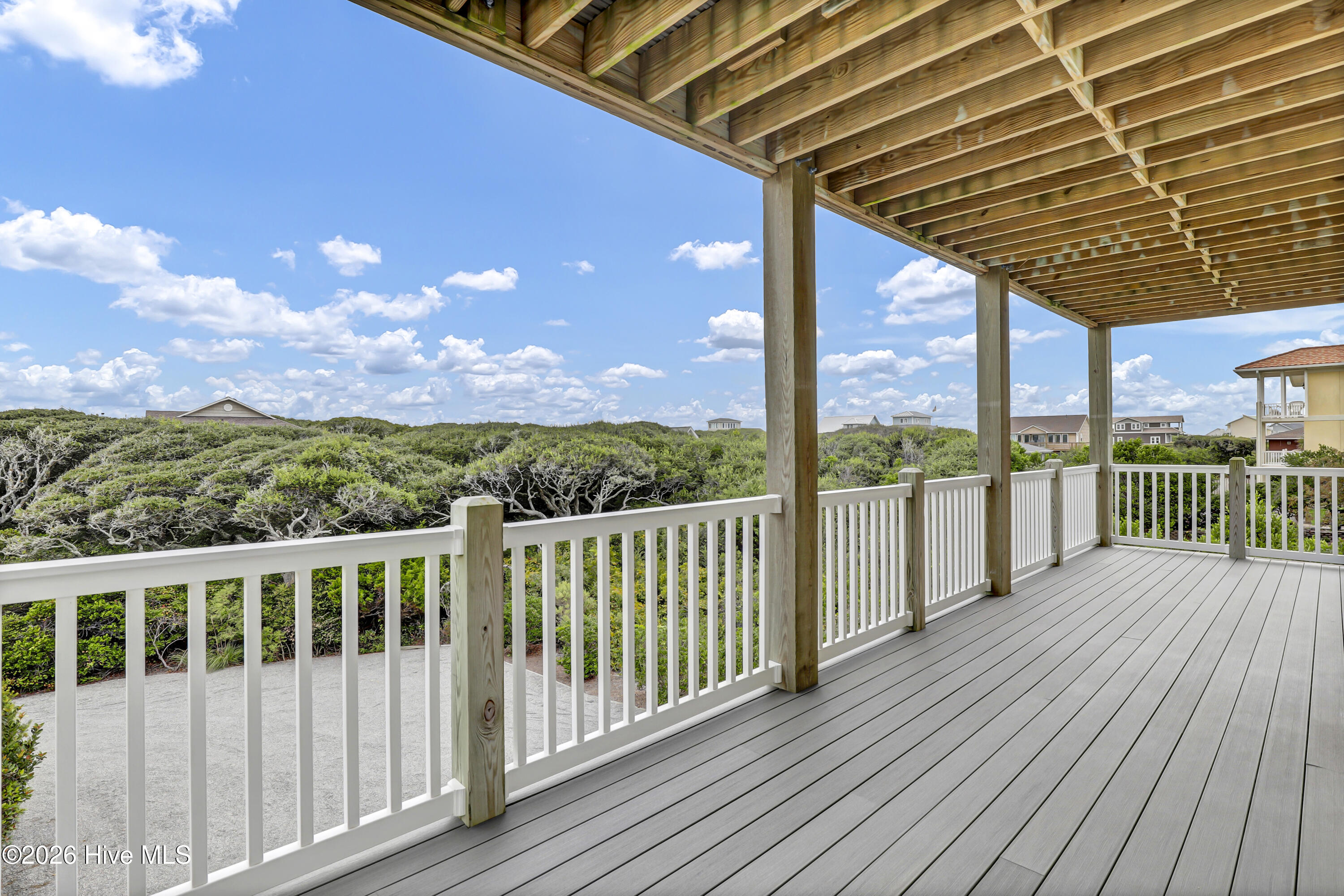 Covered deck with white railings and timber framing overlooking coastal greenery and nearby homes.