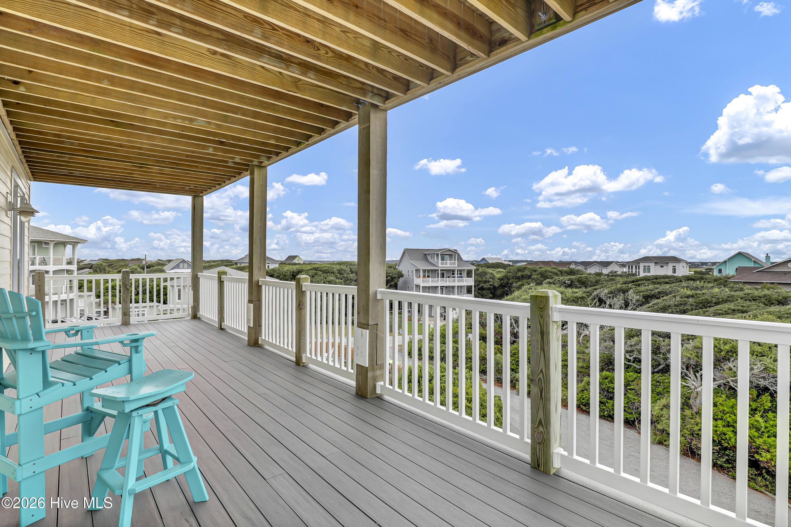 Covered deck with turquoise Adirondack chairs overlooking coastal greenery and neighboring homes.