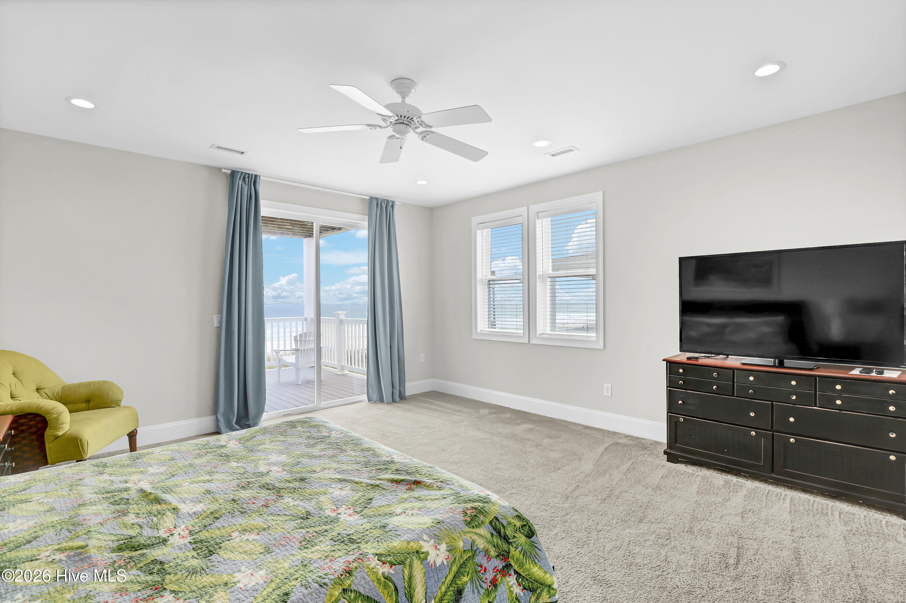 Bedroom with floral quilt and ocean-view balcony through sliding glass doors.