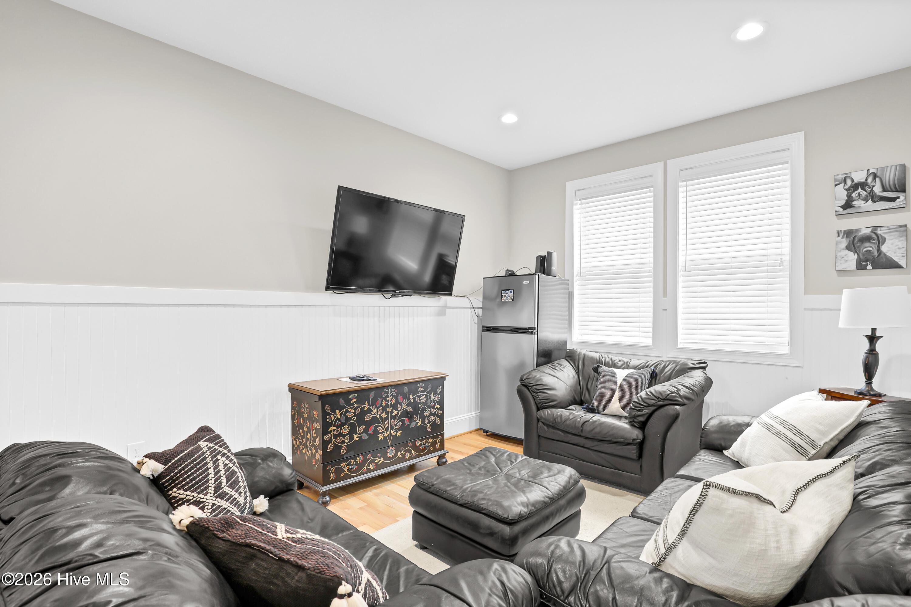Furnished living room with dark leather seating, a wall-mounted TV, and a painted chest.