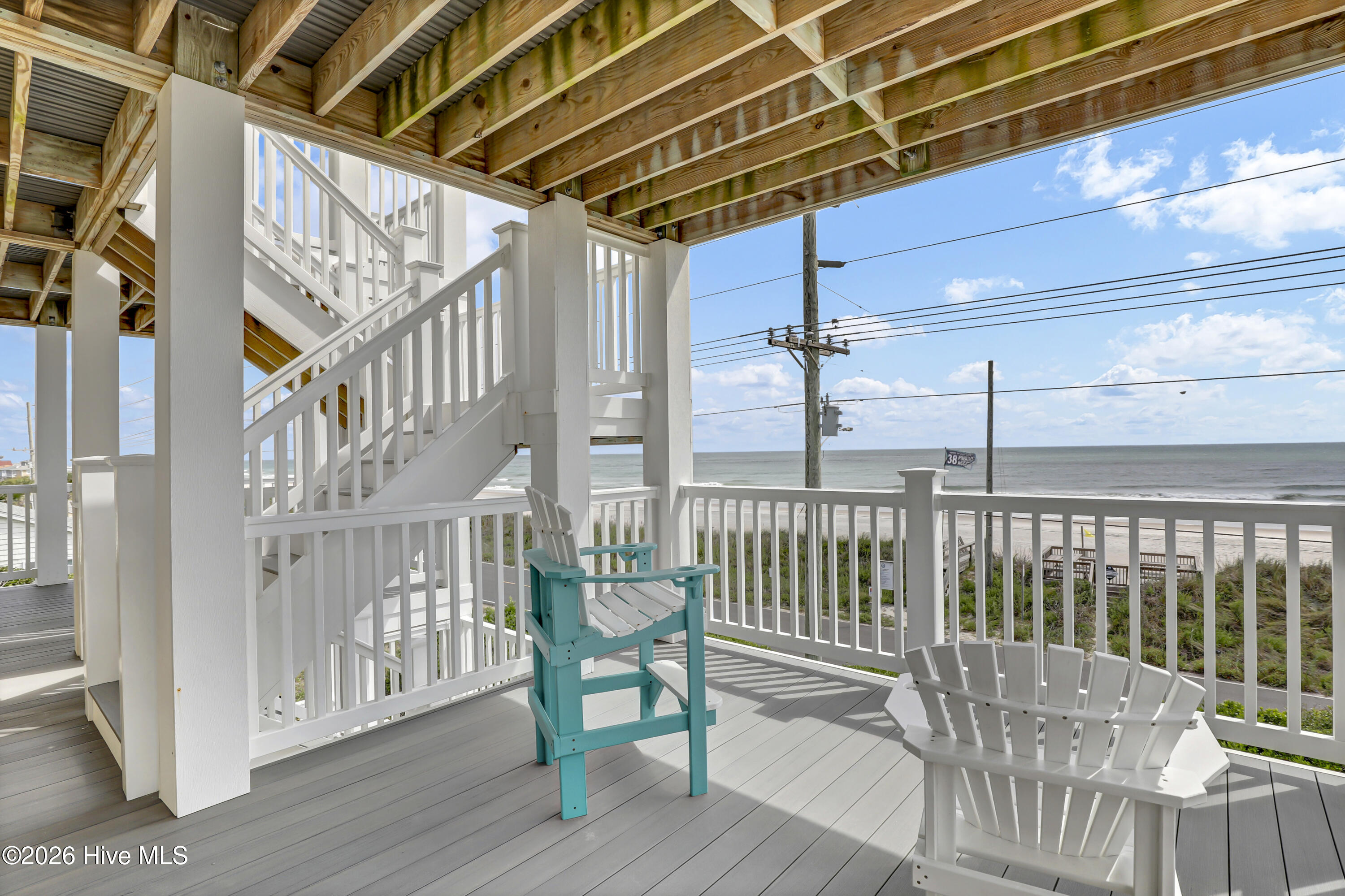 Covered deck with Adirondack chairs overlooking the beach and ocean.