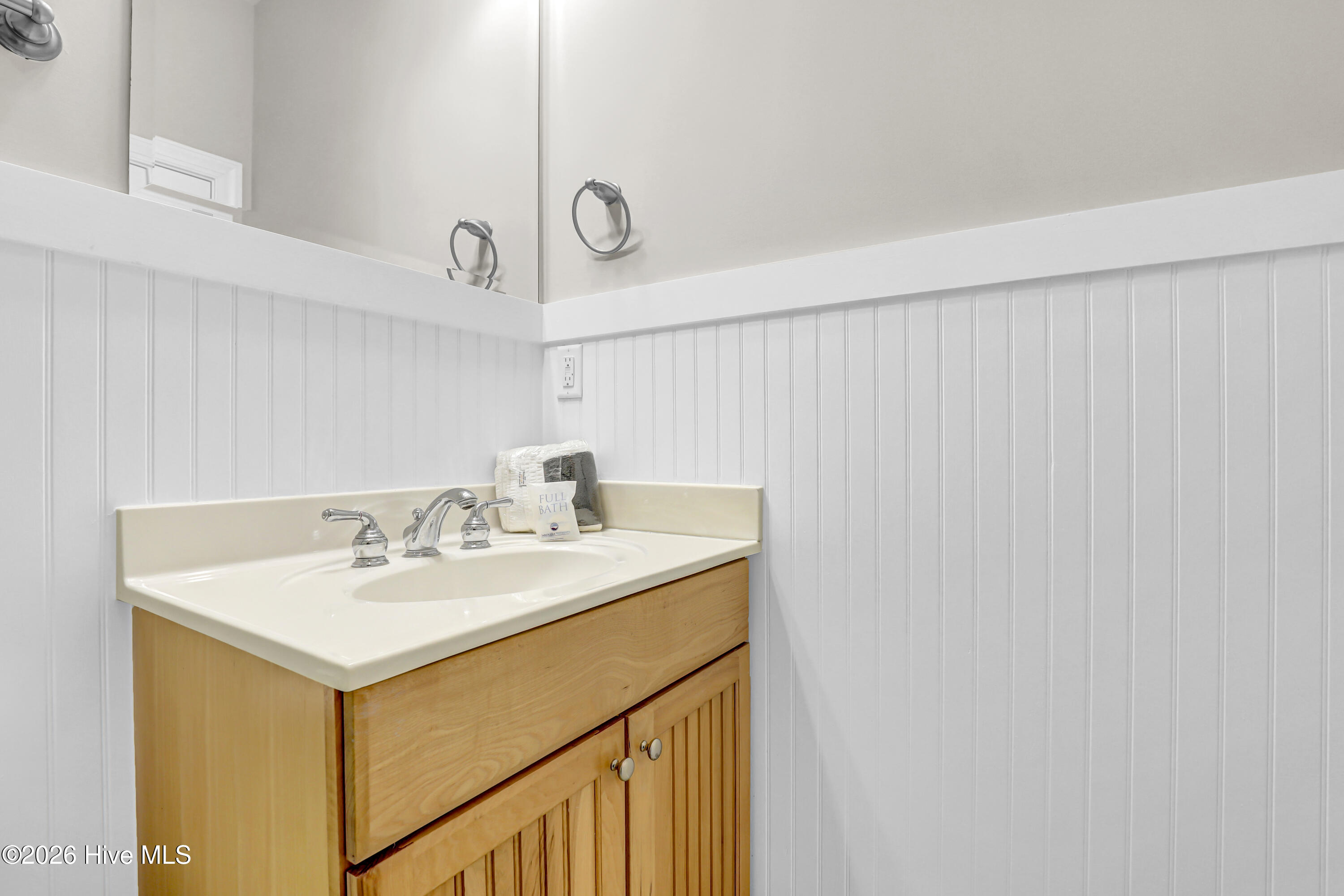 Bathroom vanity with a light wood cabinet, cream sink countertop, large mirror, and white beadboard walls.