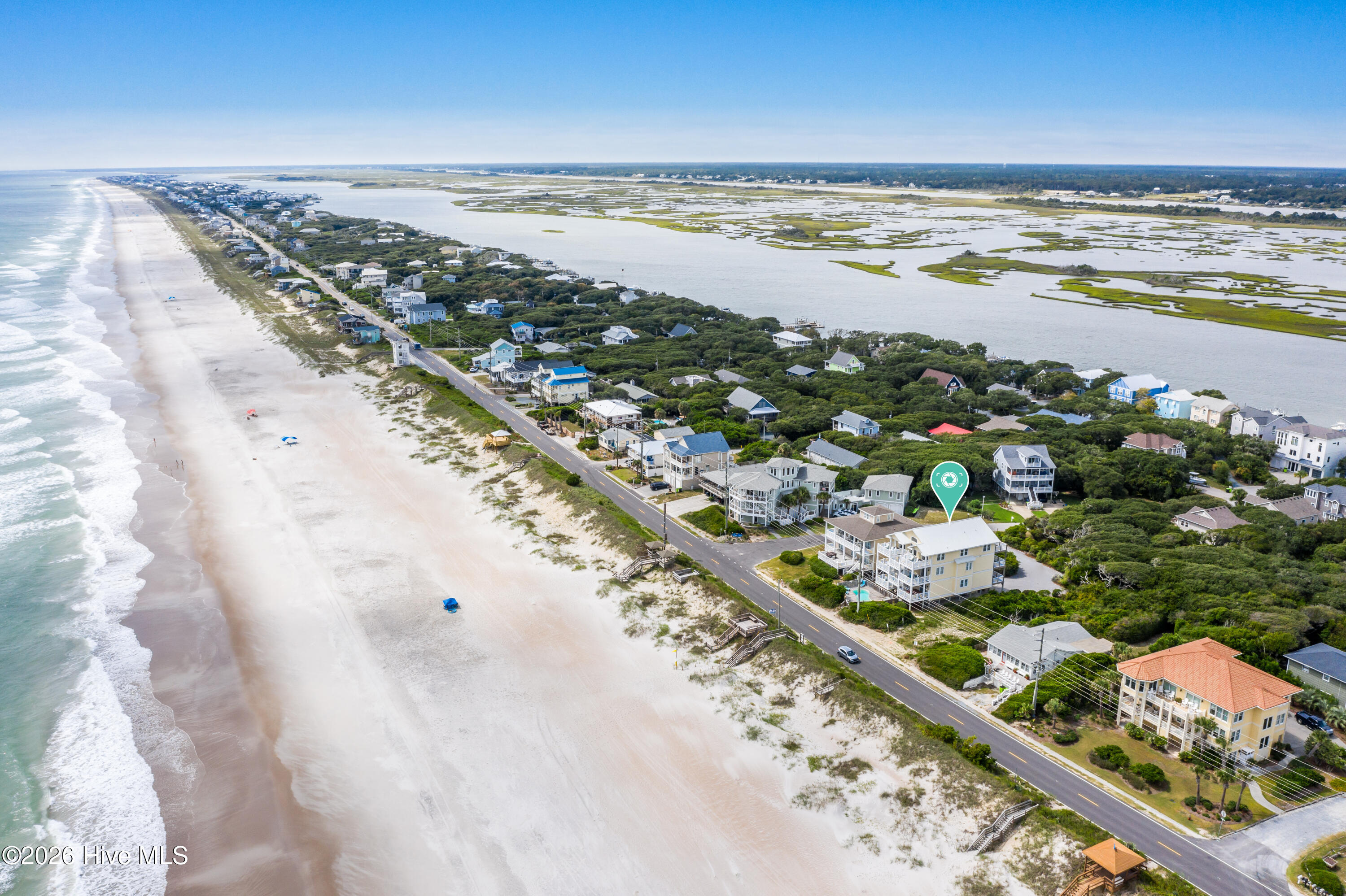 Aerial view of a coastal home near a sandy beach, ocean, and tidal marshes.