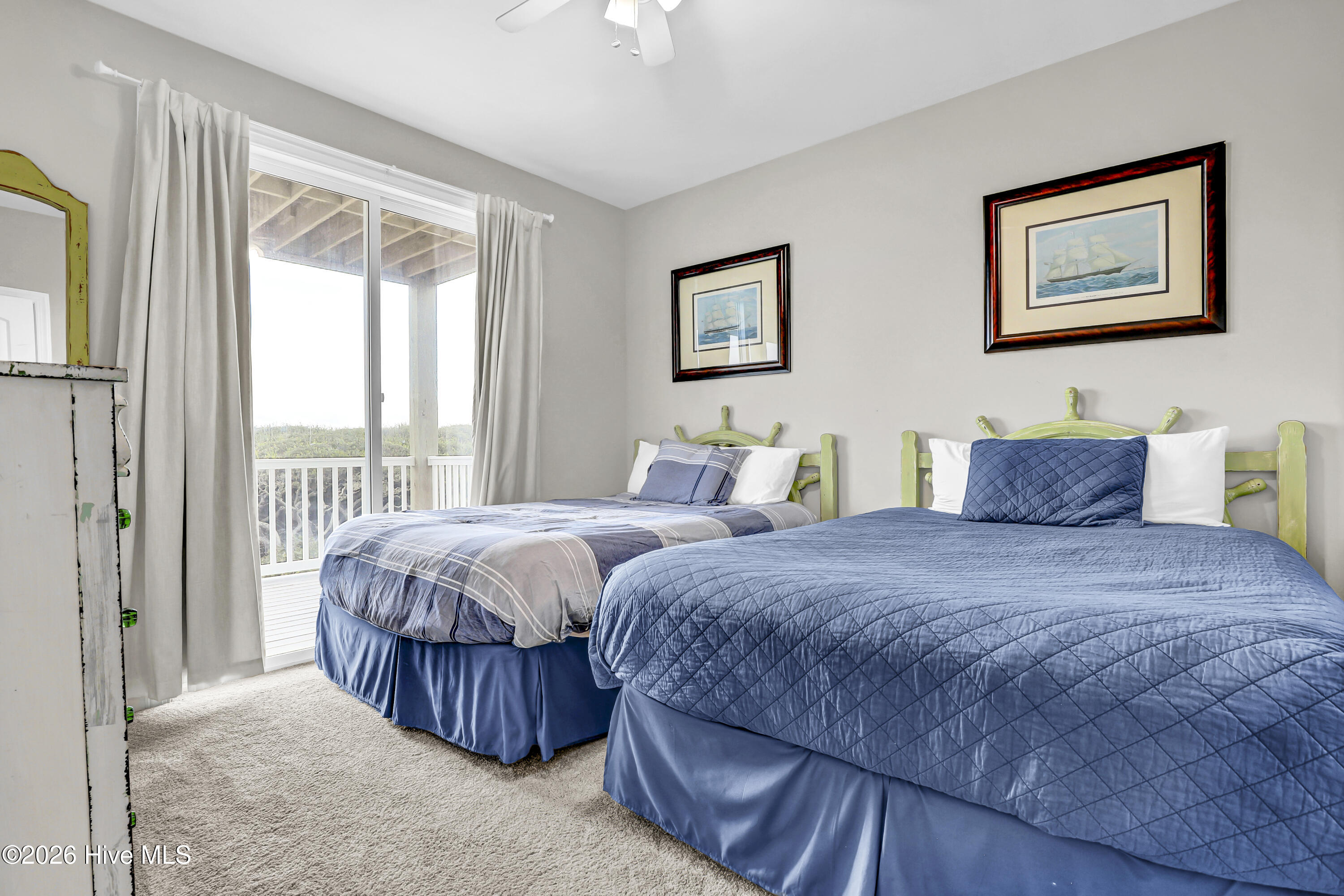 Bedroom with two blue-covered beds, green ship-wheel headboards, and a sliding door to the balcony.