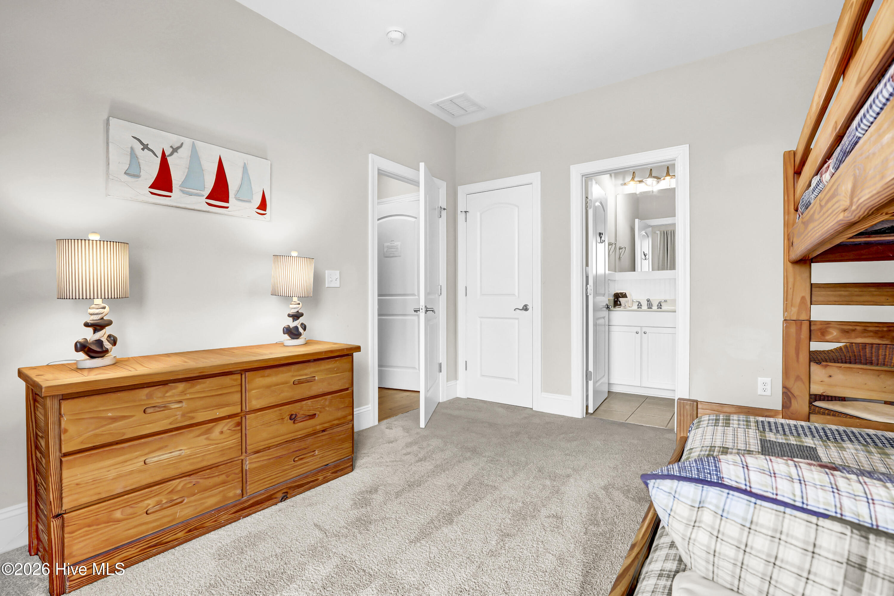 Furnished bedroom with wooden bunk beds, plaid bedding, and sailboat wall art above a dresser.