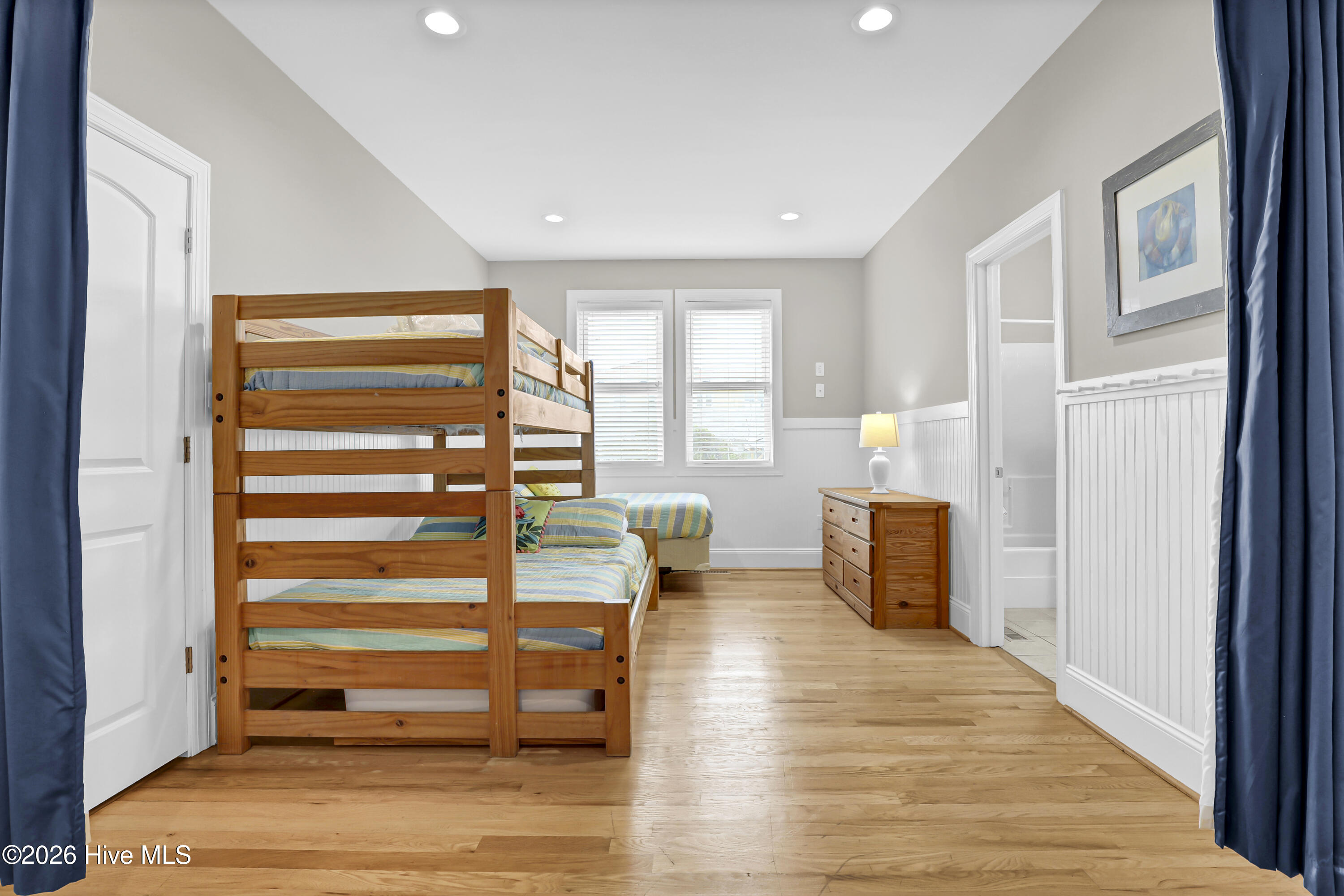 Bedroom with a wooden bunk bed, striped bedding, hardwood floors, and a dresser.
