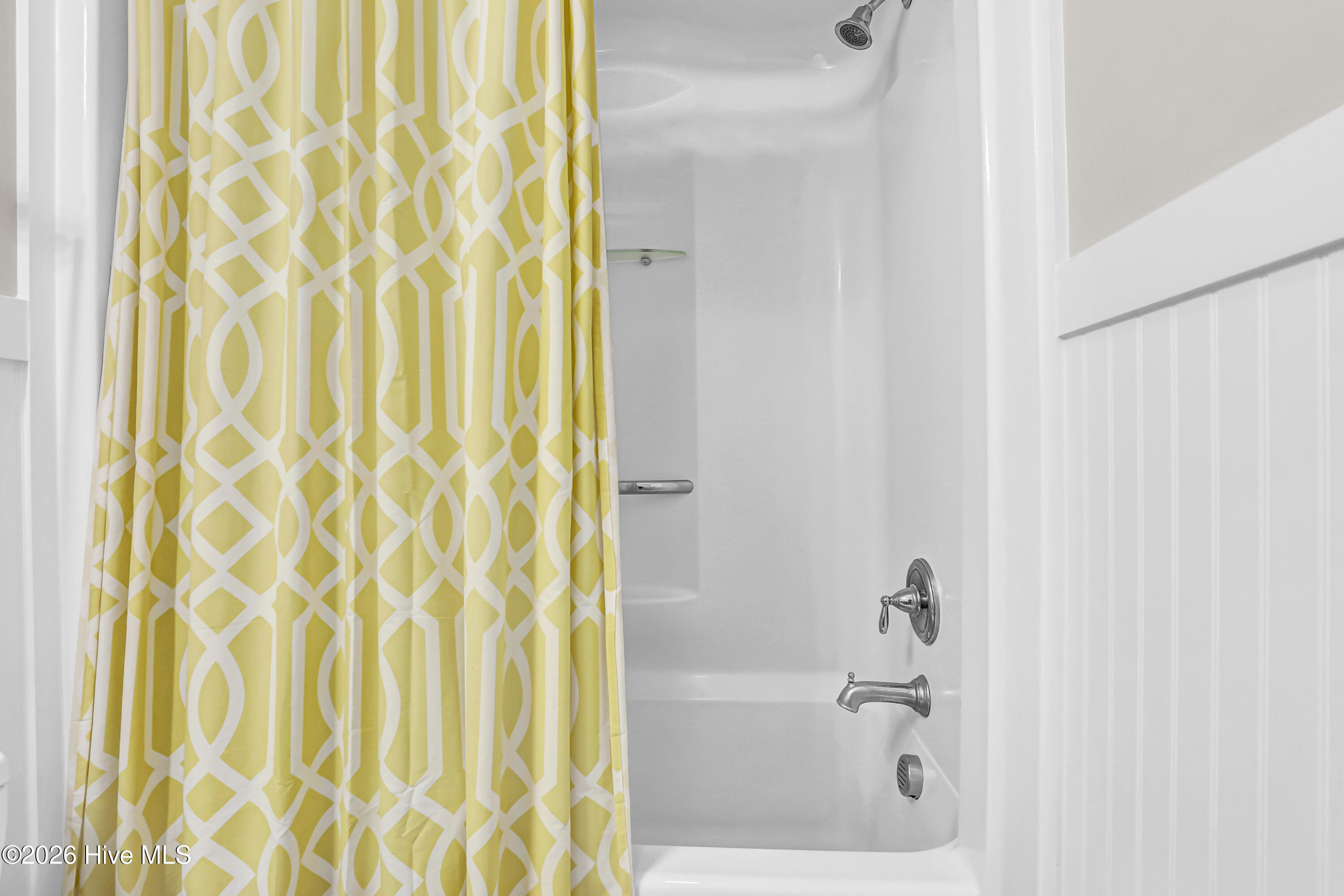 White bathtub and shower with chrome fixtures behind a yellow-and-white geometric curtain.
