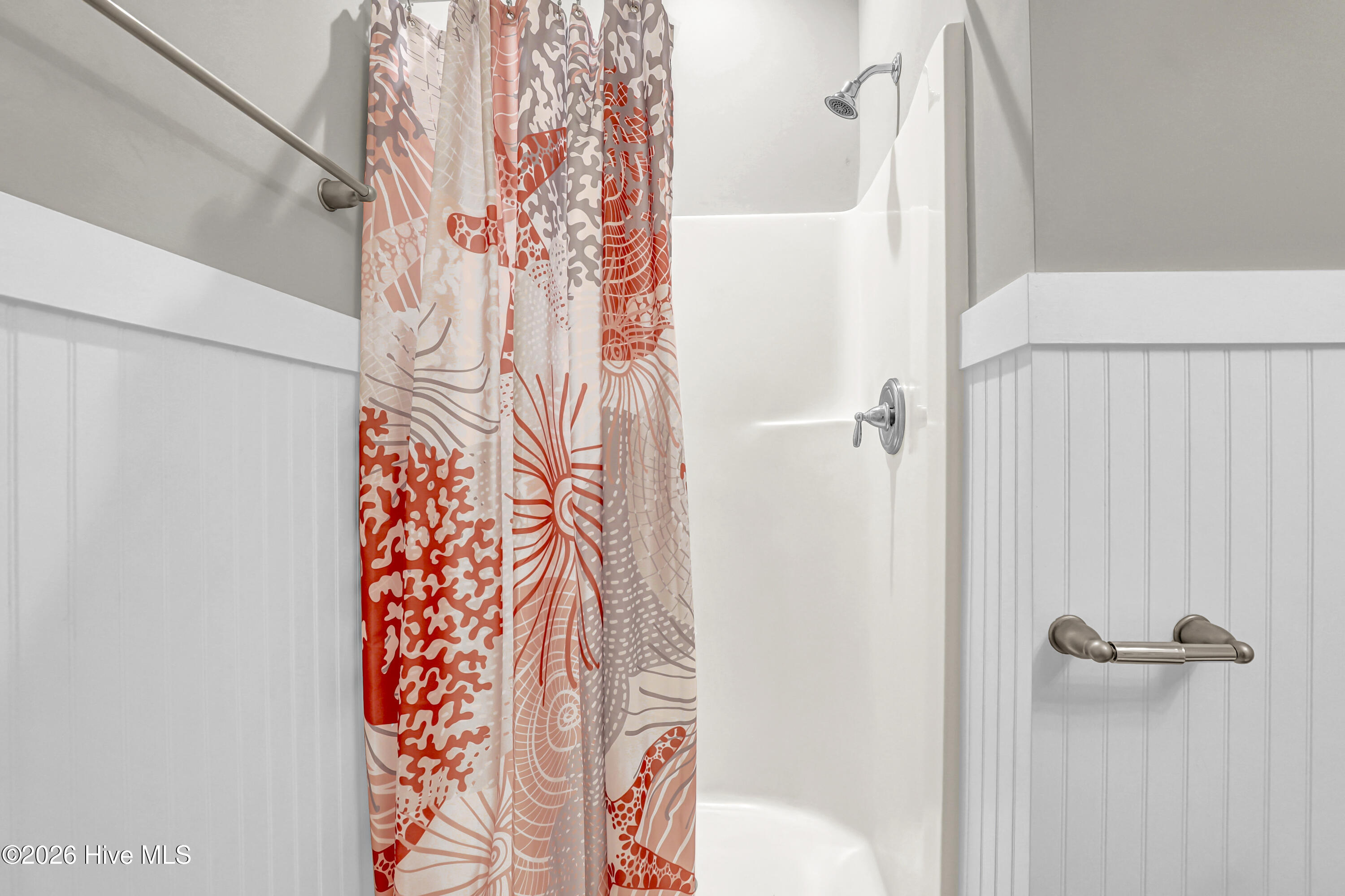 White tub and shower with a coral-patterned curtain, chrome fixtures, and a grab bar.