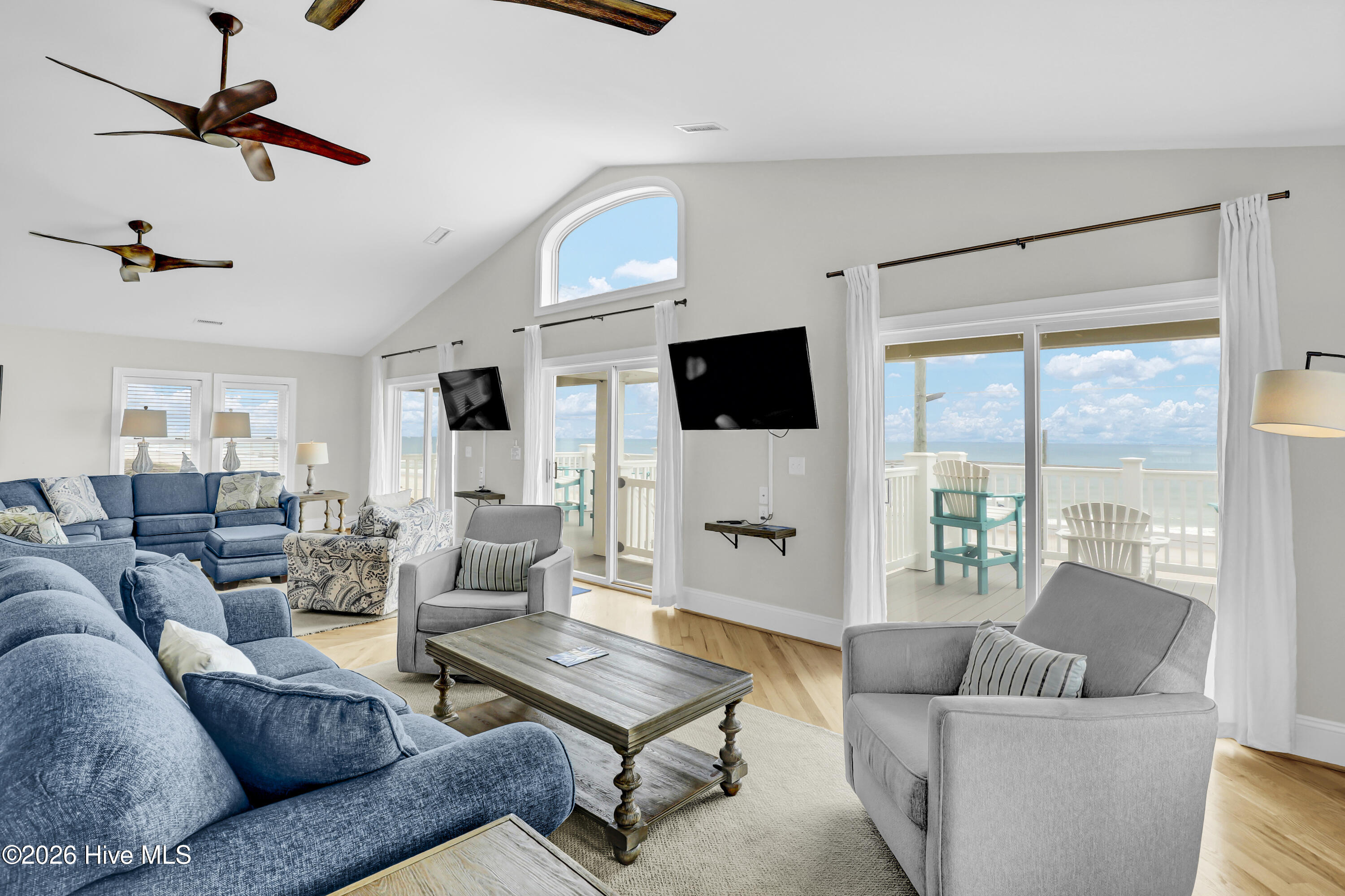 Oceanfront living room with blue sofas, gray armchairs, and sliding doors to a deck overlooking the water.