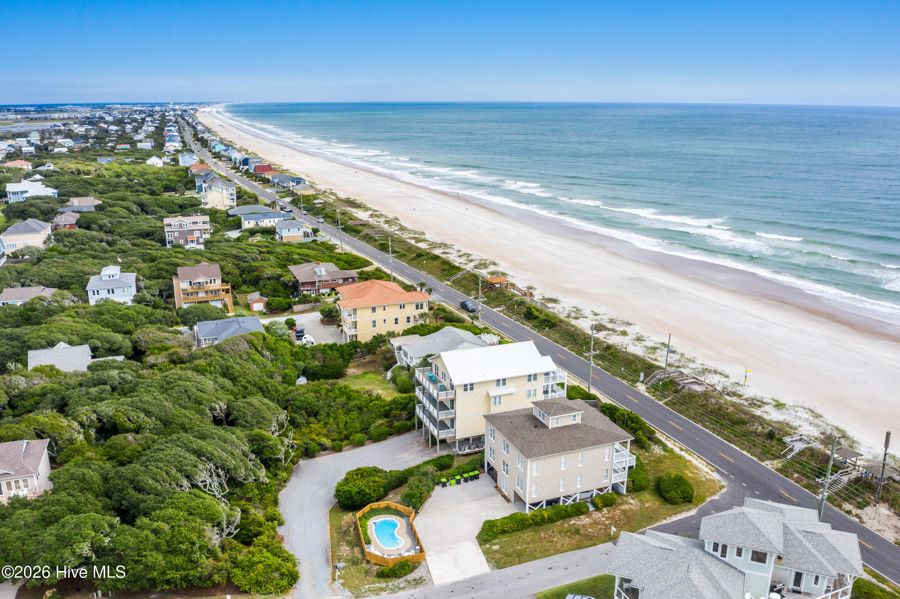 Aerial view of beachside homes, with a fenced pool beside a multi-story house.