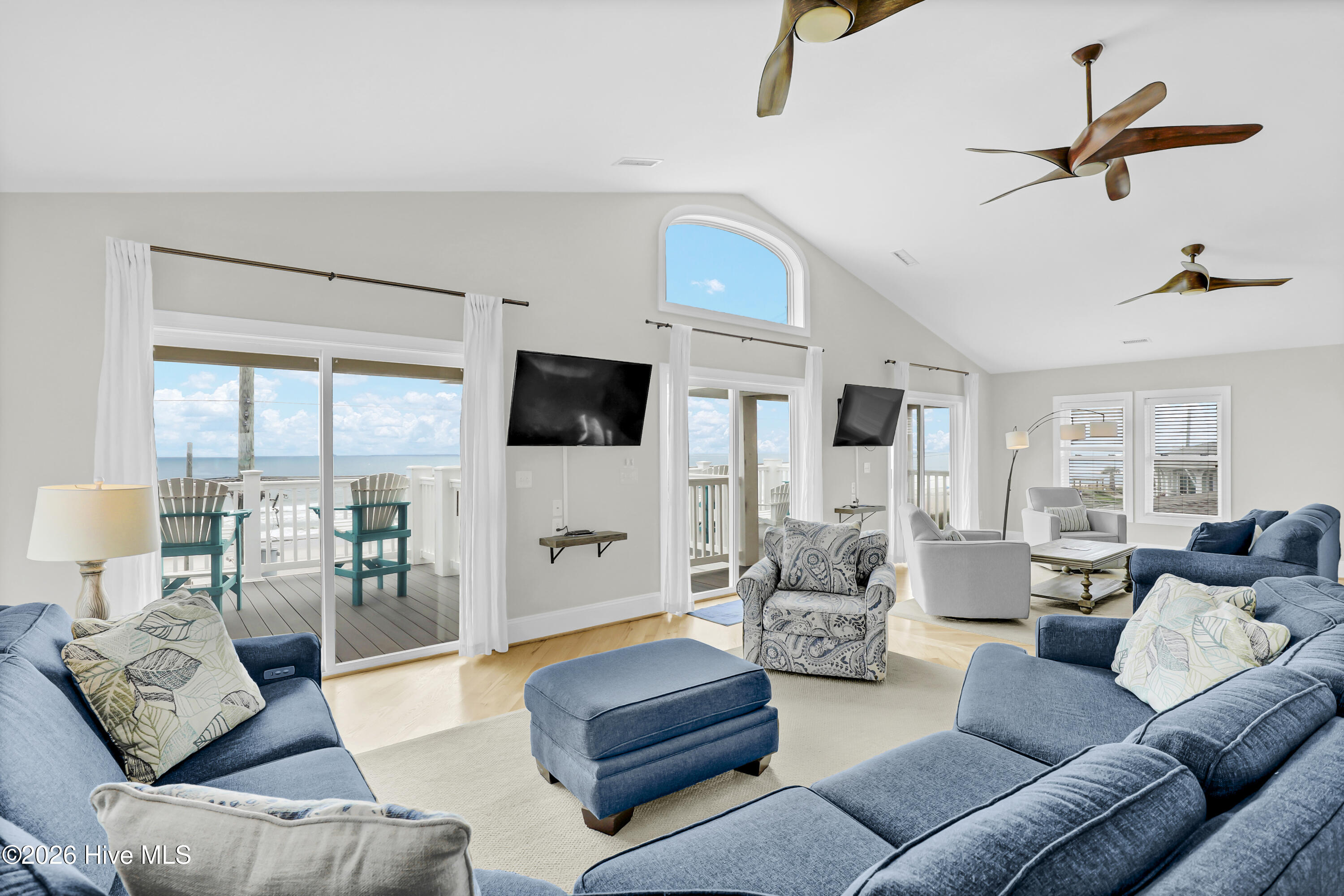 Furnished living room with vaulted ceiling, blue sofas, and sliding doors overlooking the ocean.
