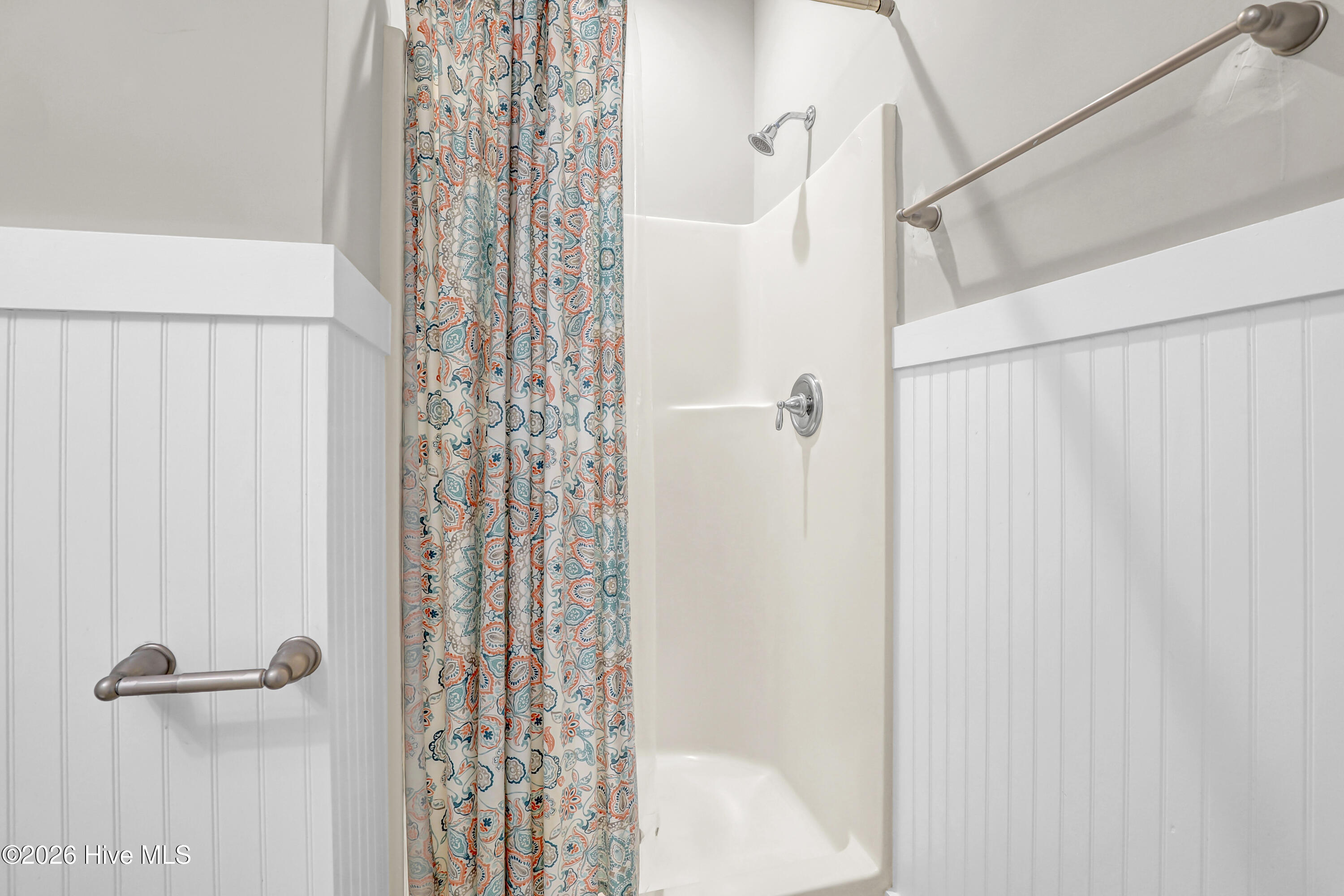 Bathroom with a white tub and shower, chrome fixtures, and a colorful patterned curtain.