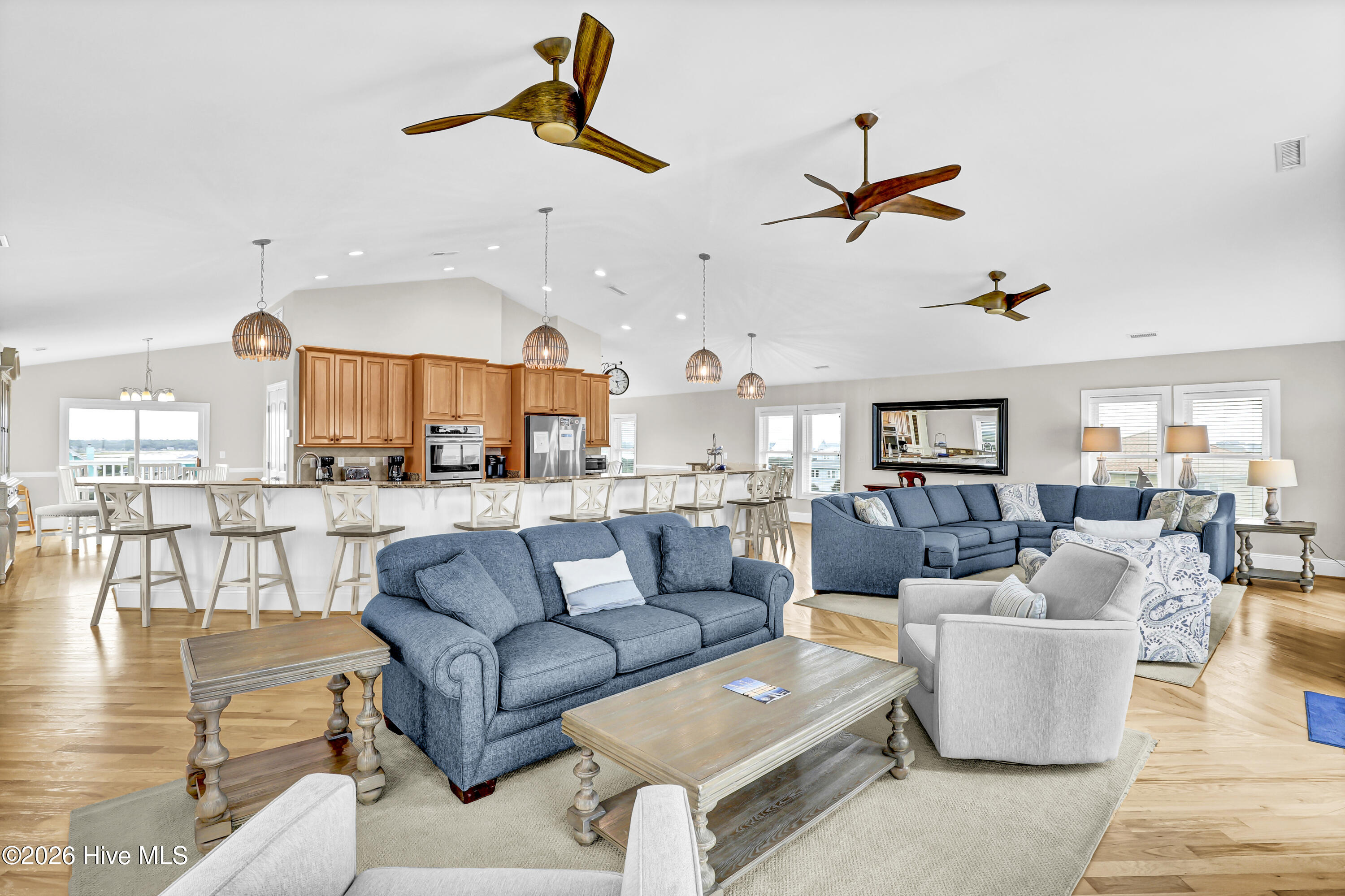 Open-plan living room and kitchen with blue sofas, a large island, hardwood floors, and water views.