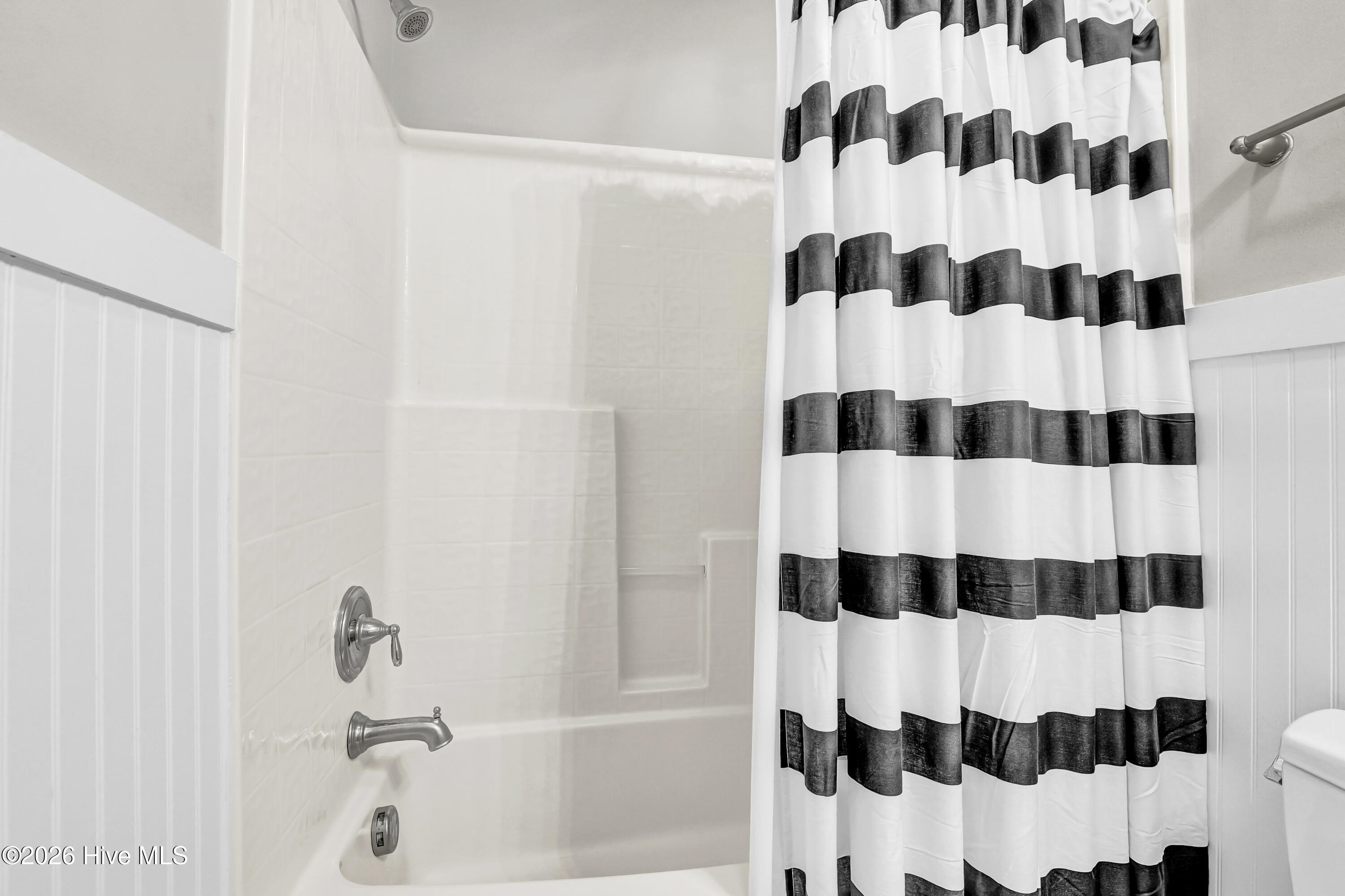 Bathroom tub and shower with chrome fixtures and a black-and-white striped curtain.