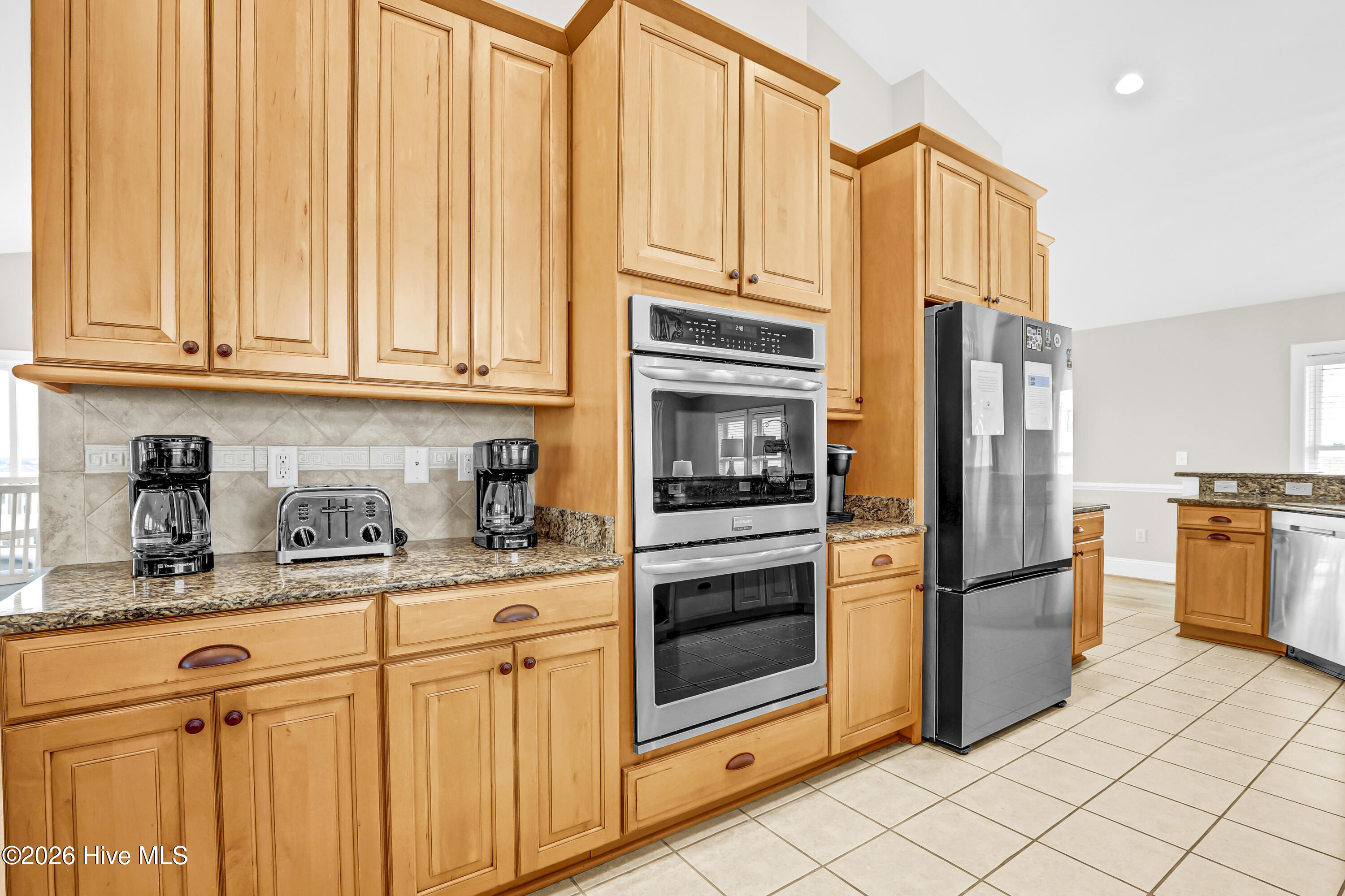 Kitchen with honey-colored cabinets, granite counters, and stainless steel double wall oven and refrigerator.
