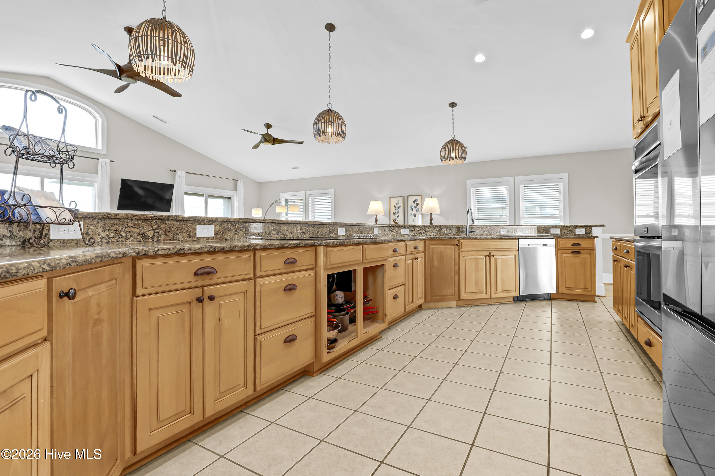 Kitchen with honey-colored cabinets, stone countertops, stainless steel appliances, and a vaulted ceiling.