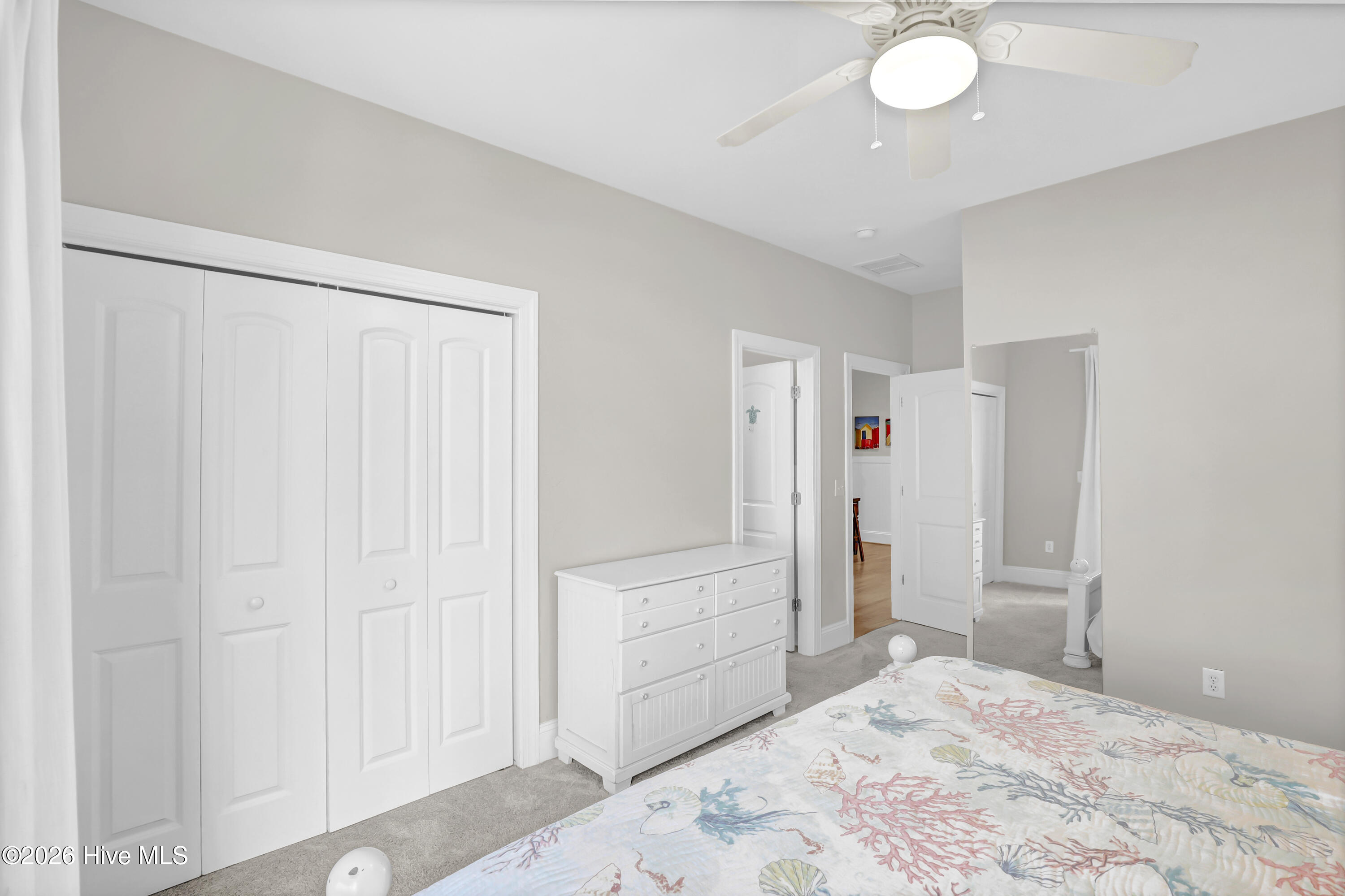 Bedroom with a coral-patterned bedspread, white dresser, and sliding closet doors.